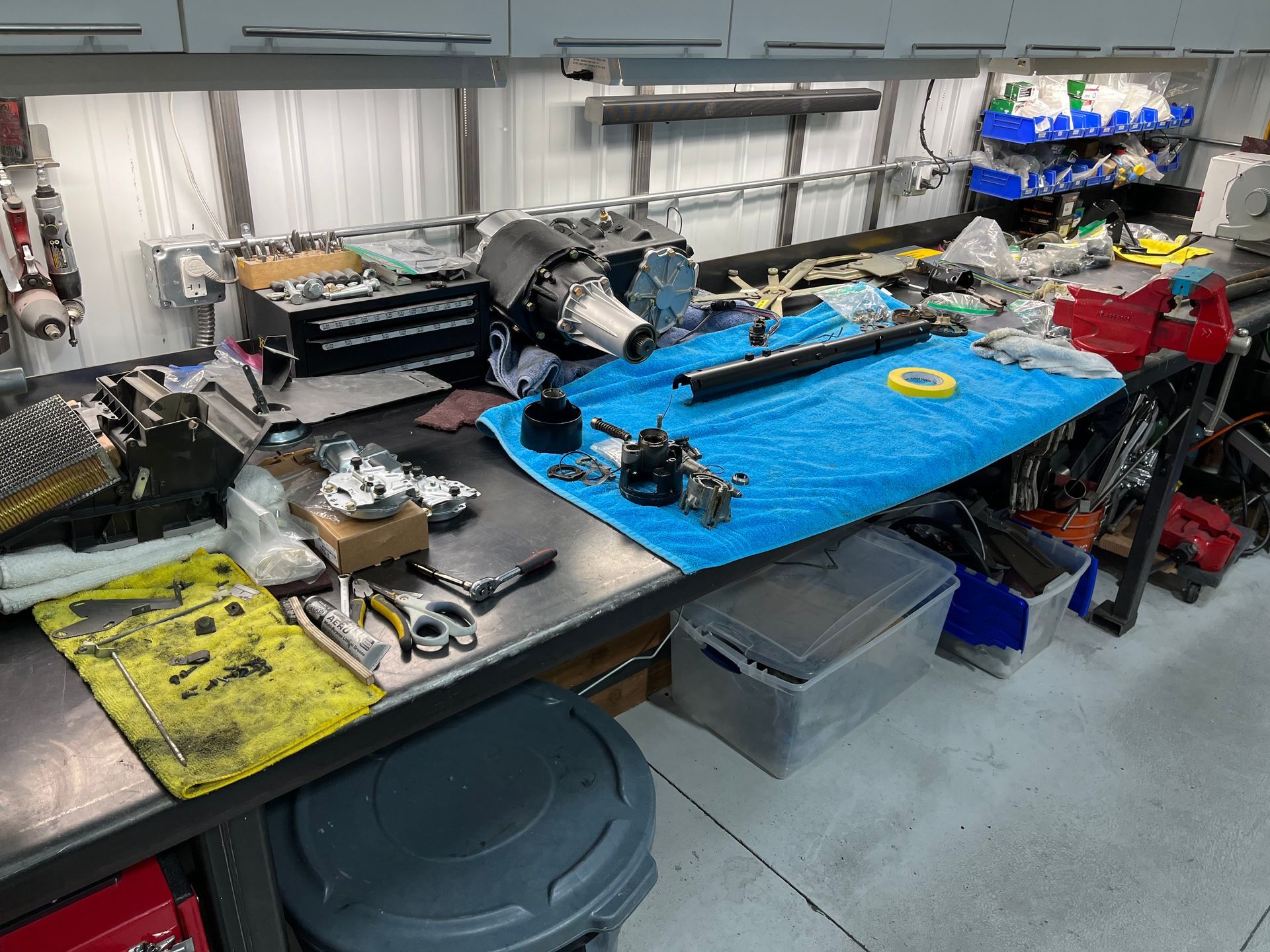 Workshop bench with parts and tools laid out, including a blue mat and engine components in a garage-like workspace.