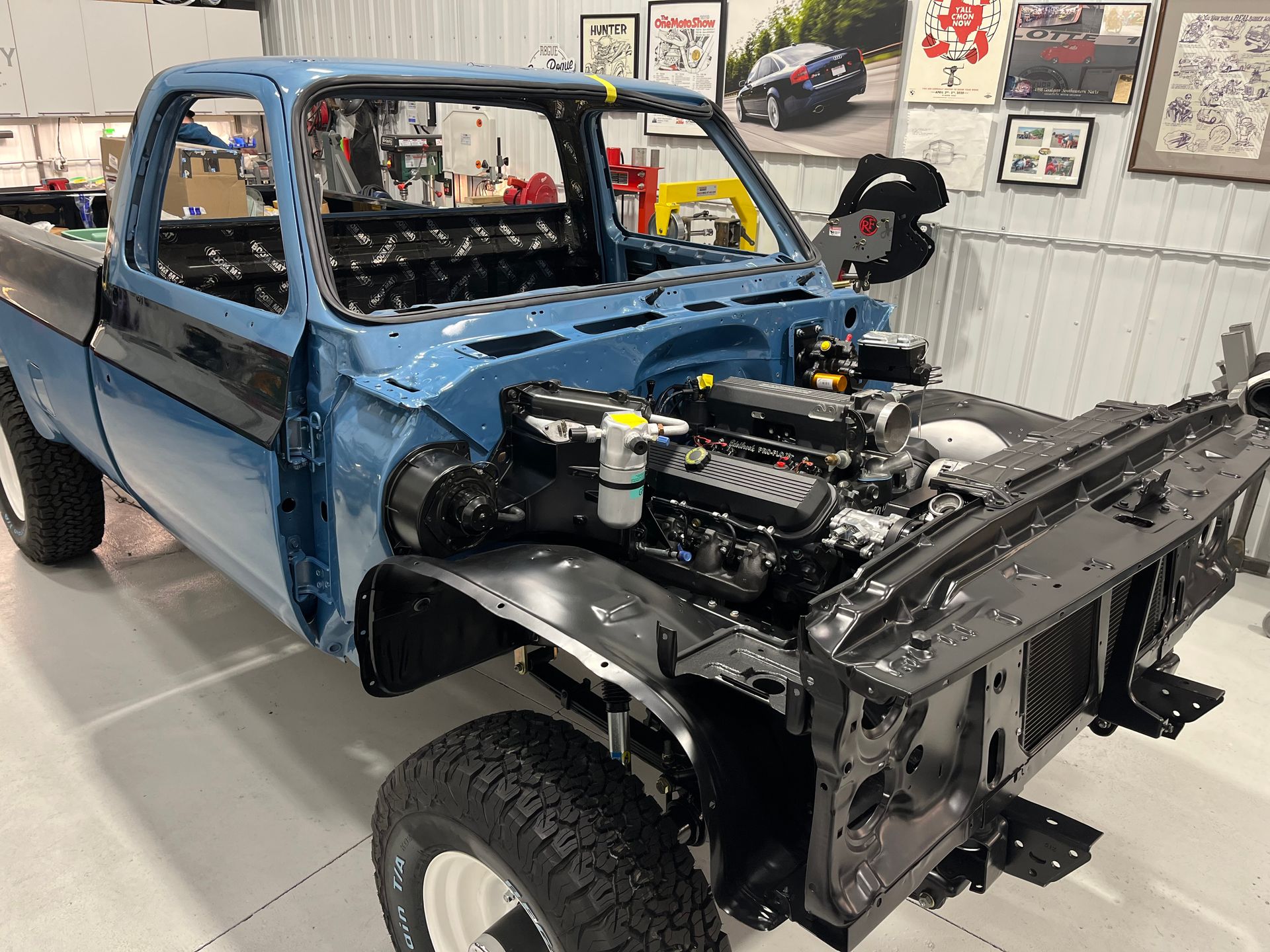Blue vintage pickup truck in a garage, front body removed and engine exposed on a chassis.