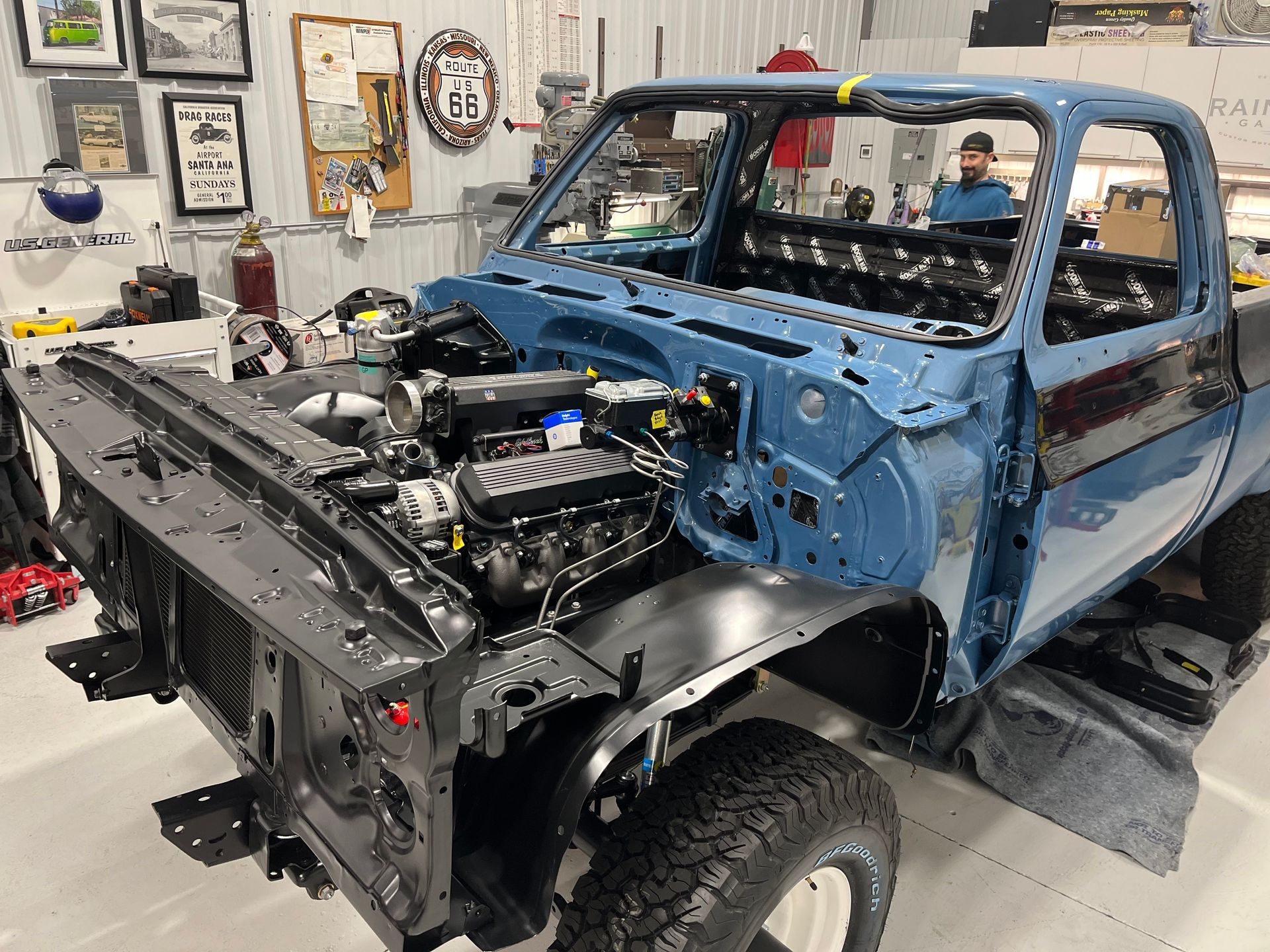 Blue off-road truck under repair in a workshop, with front body removed and engine exposed.