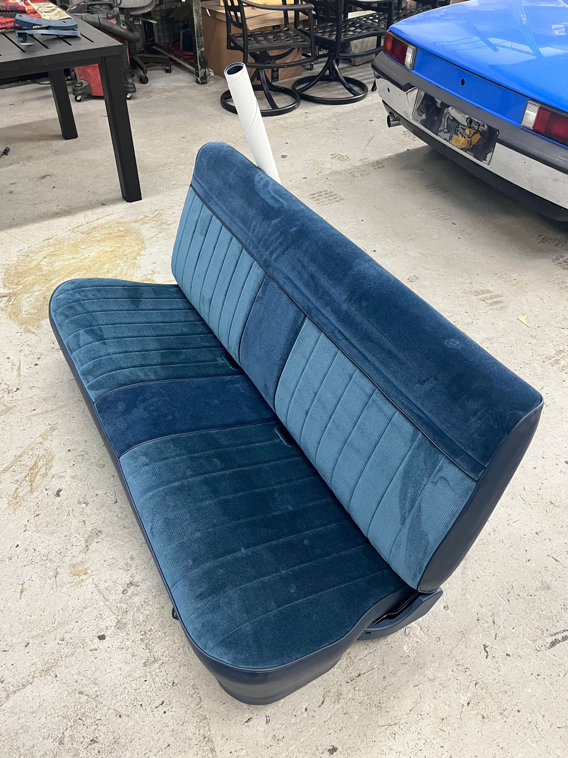Blue and teal upholstered car bench seat on a concrete floor, shown at an angle.