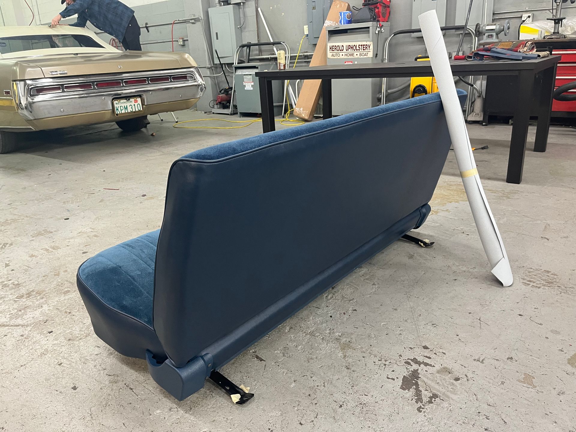 Blue upholstered bench seat in a workshop, leaning on its side next to a table and white pole