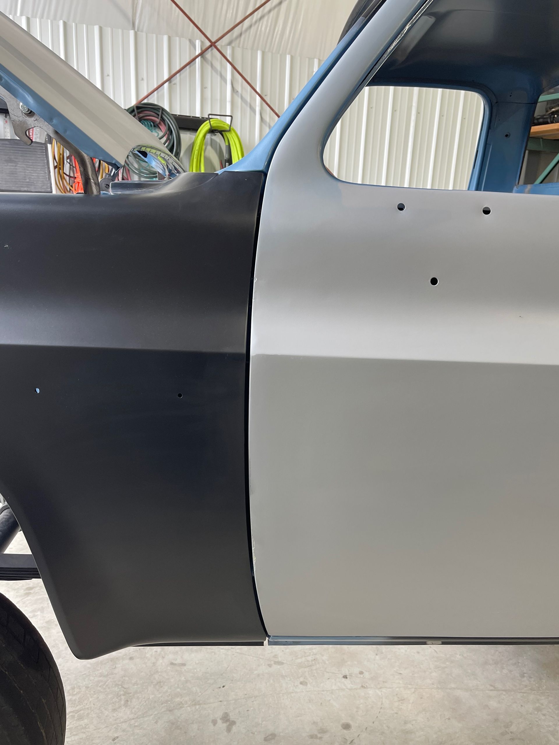 Two-tone black and gray car body in a garage, showing the side panel and rear window area