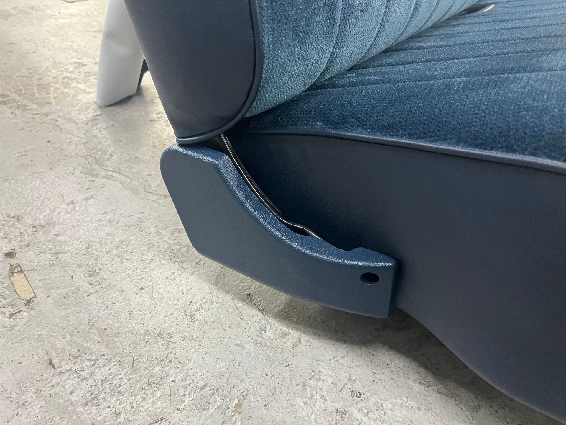 Blue upholstered seat armrest with a small black screw hole beside a gray carpeted floor.