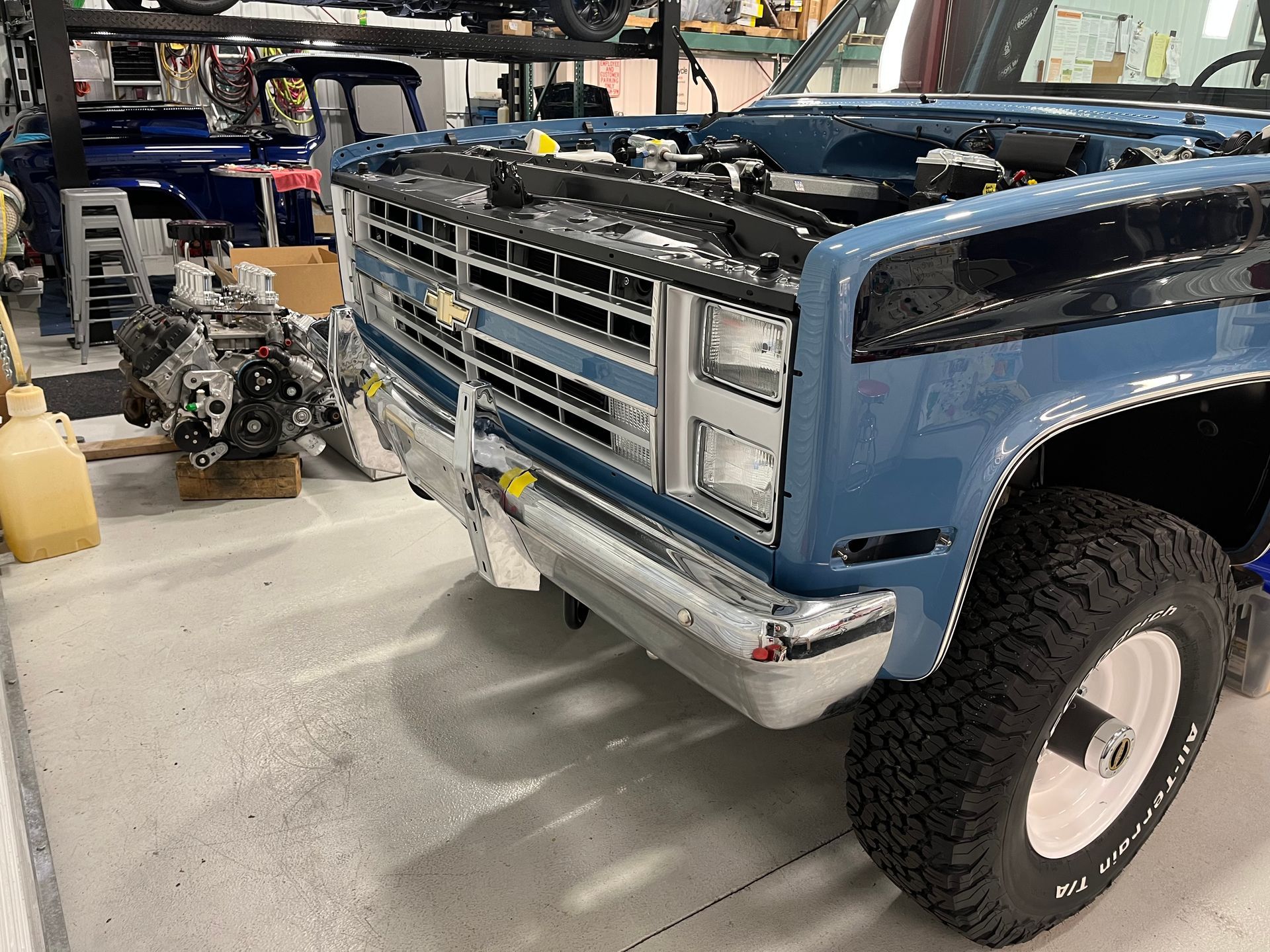 Blue vintage truck in a garage, front grille exposed with parts and tools nearby.