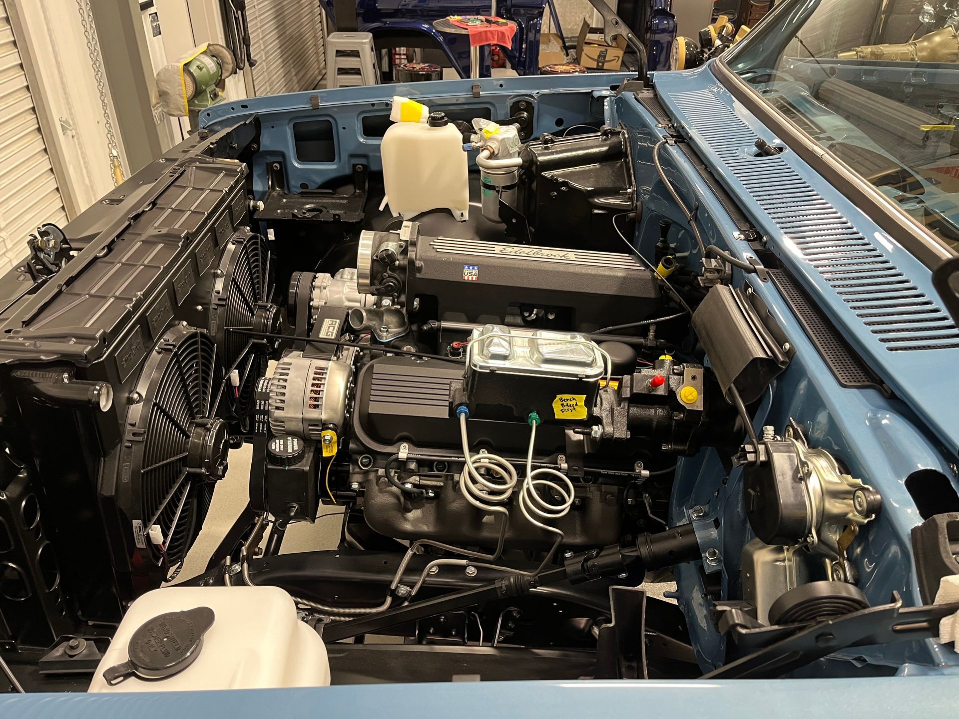 Open car hood showing a compact engine bay with blue body panels and exposed components.