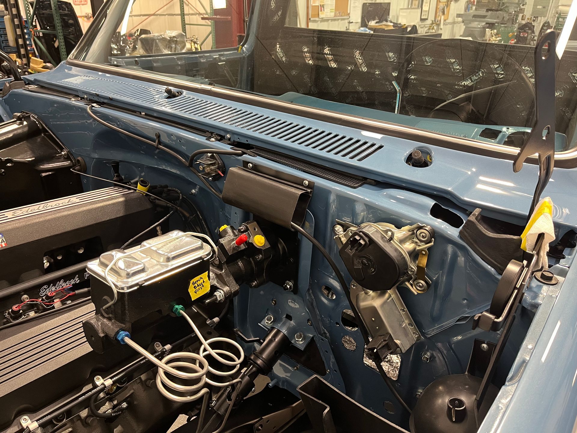 Blue car interior with exposed dashboard, wiring, and engine bay components under the windshield.