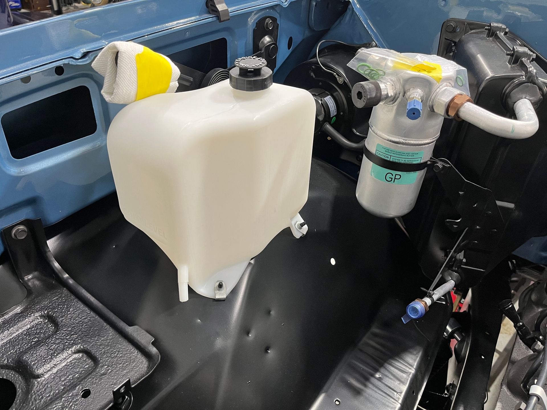 Vehicle interior with a mounted white fluid reservoir and hoses beside a black seat.