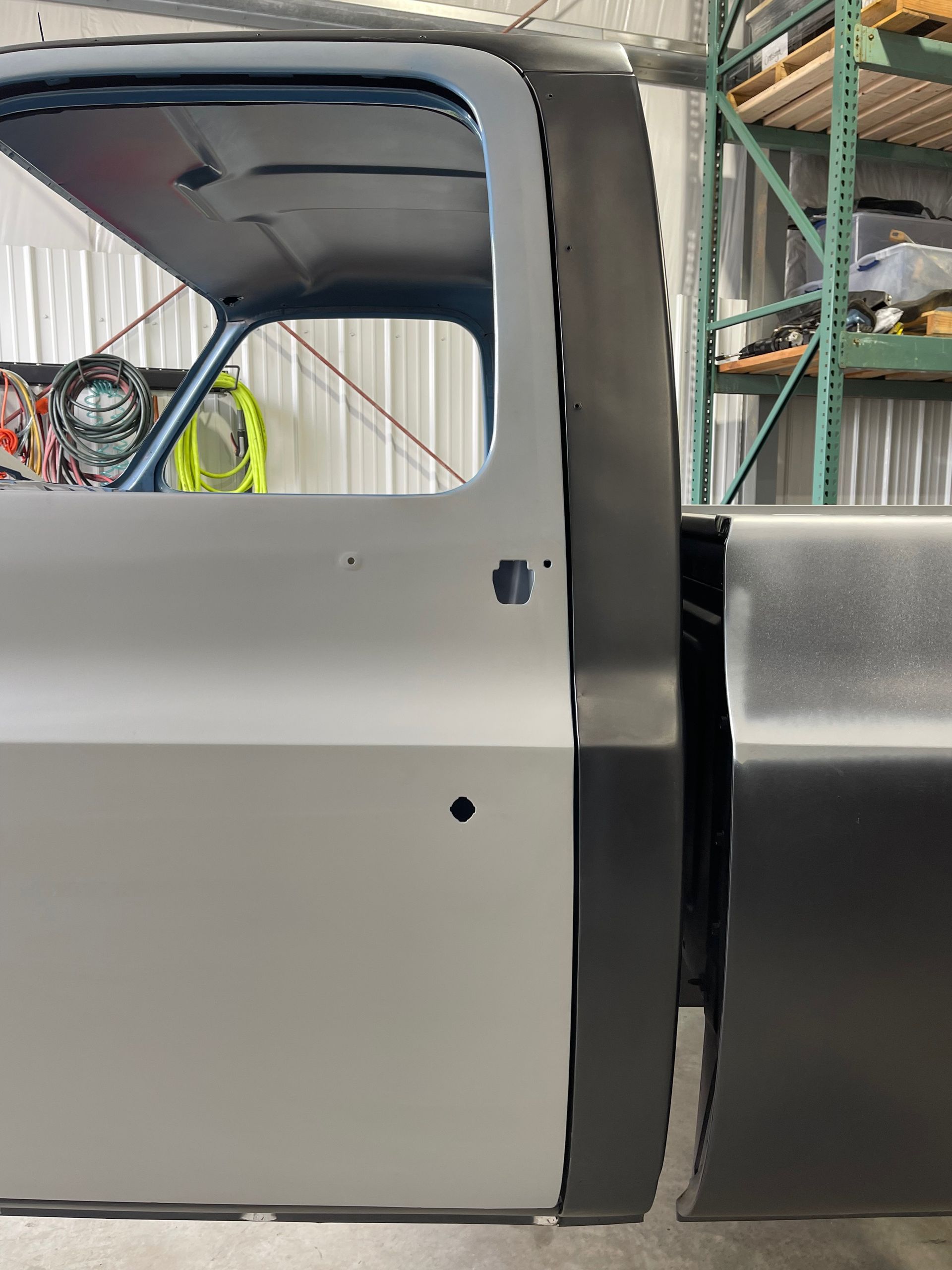 Partially assembled silver car body in a workshop, showing the side door area and rear panel