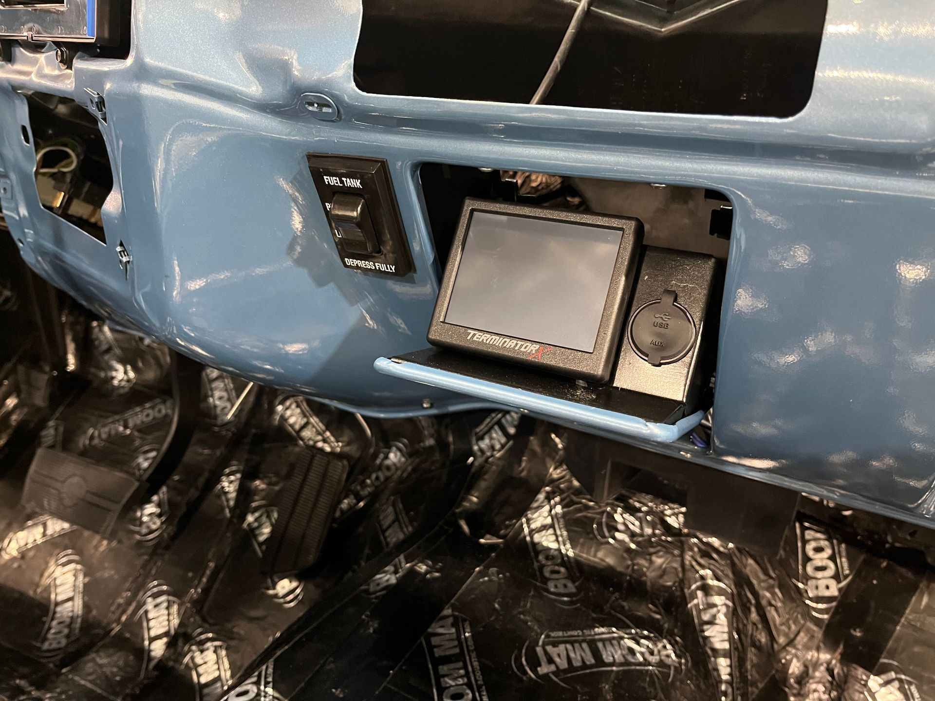 Blue vehicle bumper with a mounted display or control panel above black plastic-wrapped cargo below