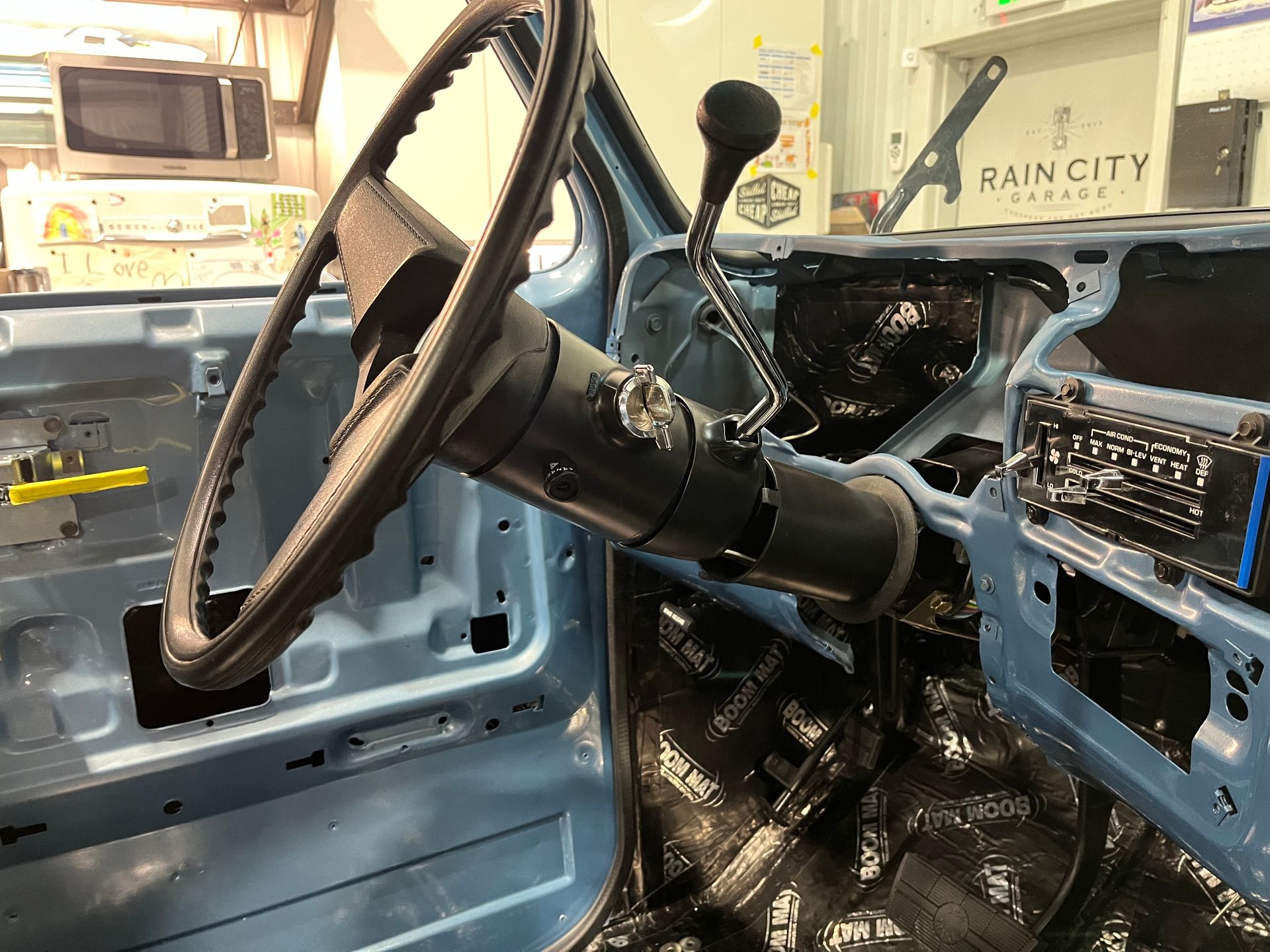 Interior of a blue vintage truck with a black steering wheel and manual gear shifter in a garage