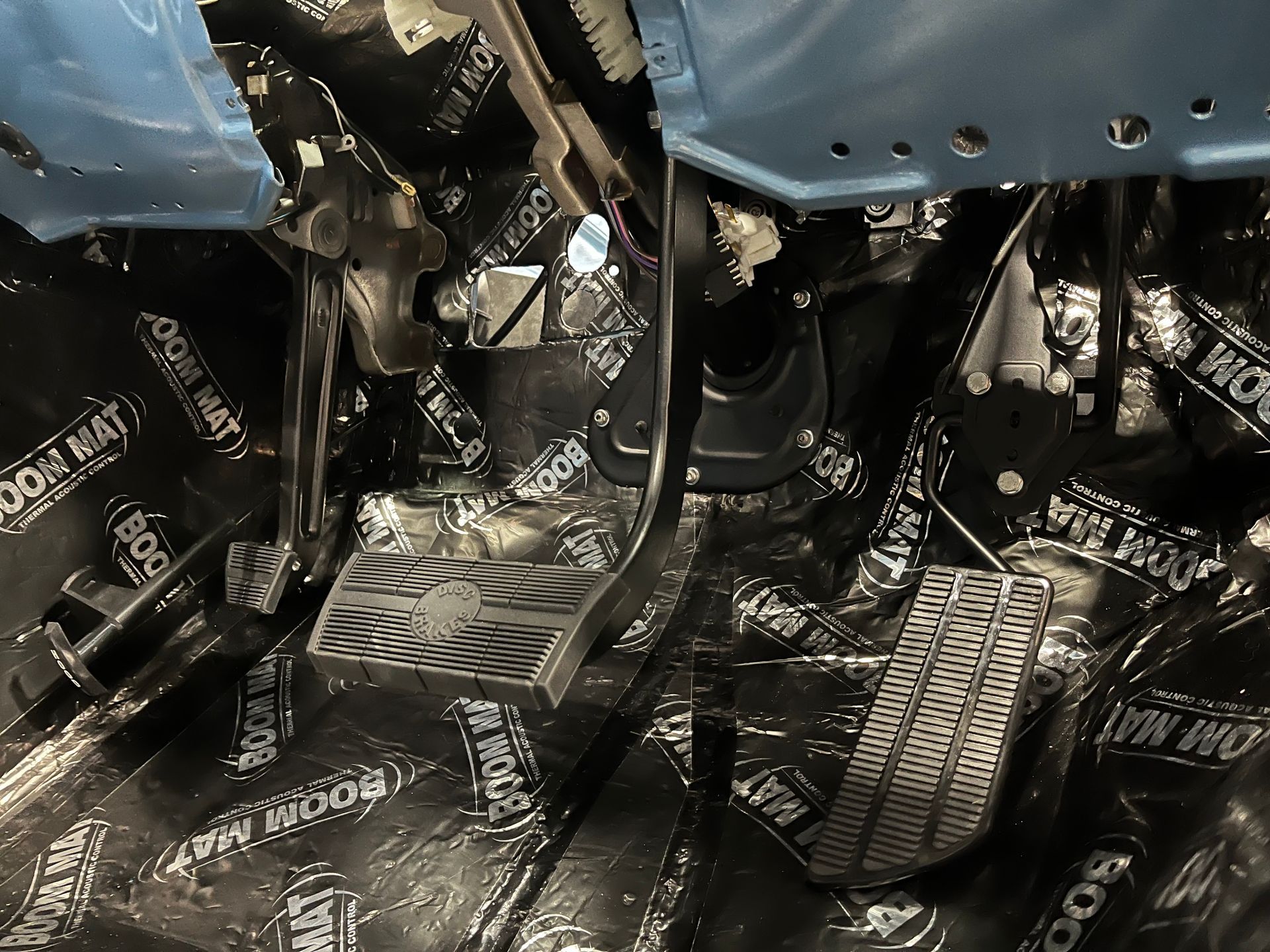 Car interior floor covered with black soundproofing mats and exposed pedals under blue seats