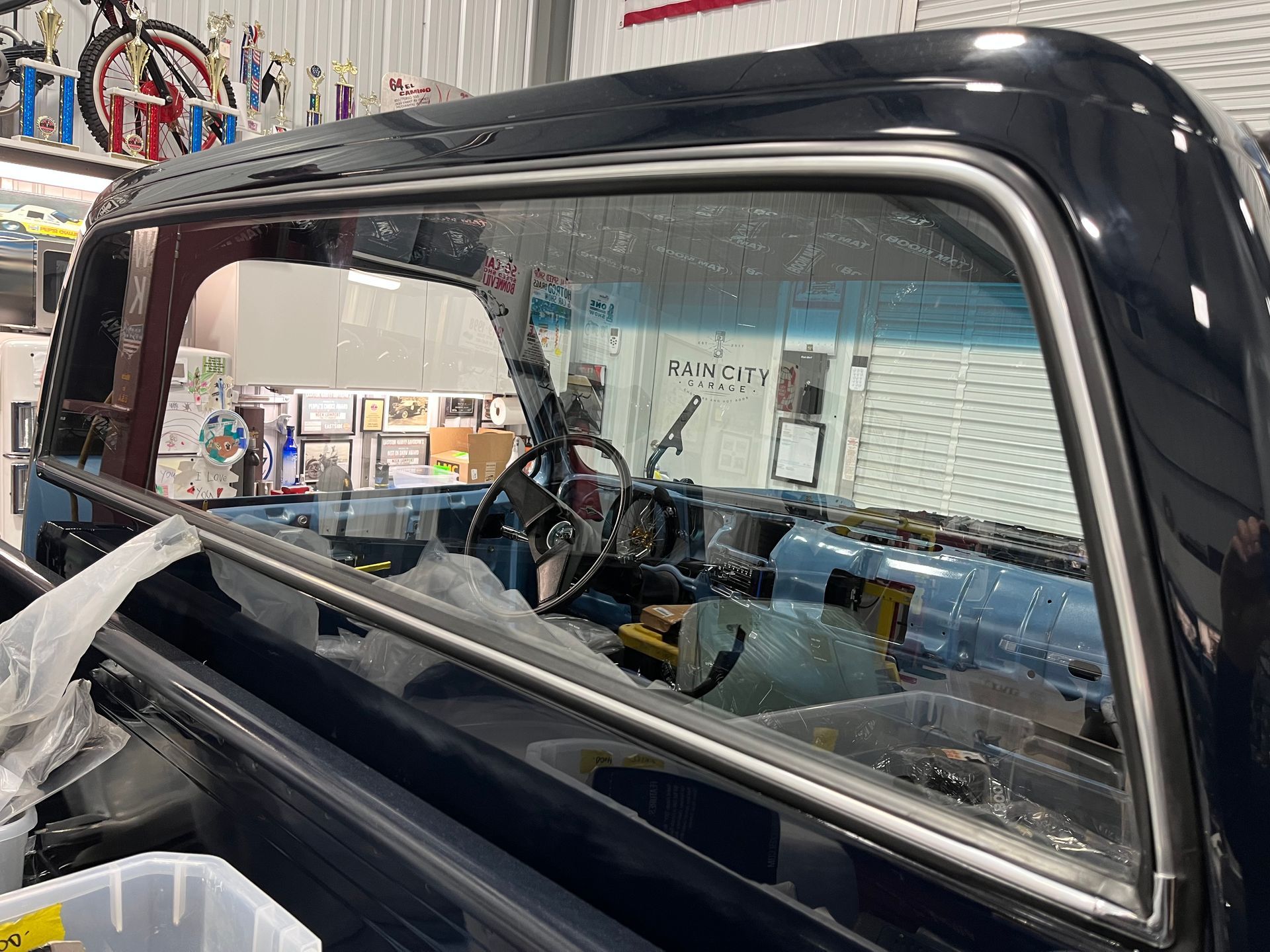Black vintage truck cab with open window in a garage, showing the steering wheel and dashboard