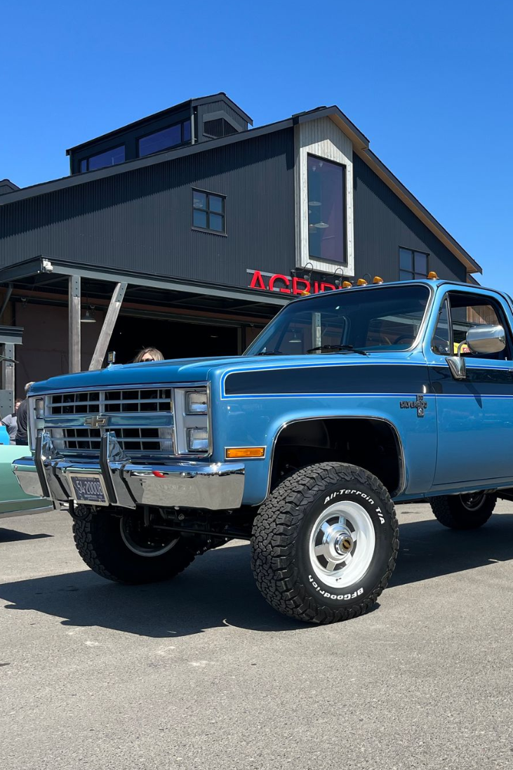Blue lifted pickup truck parked in front of a dark gray building under a clear sky