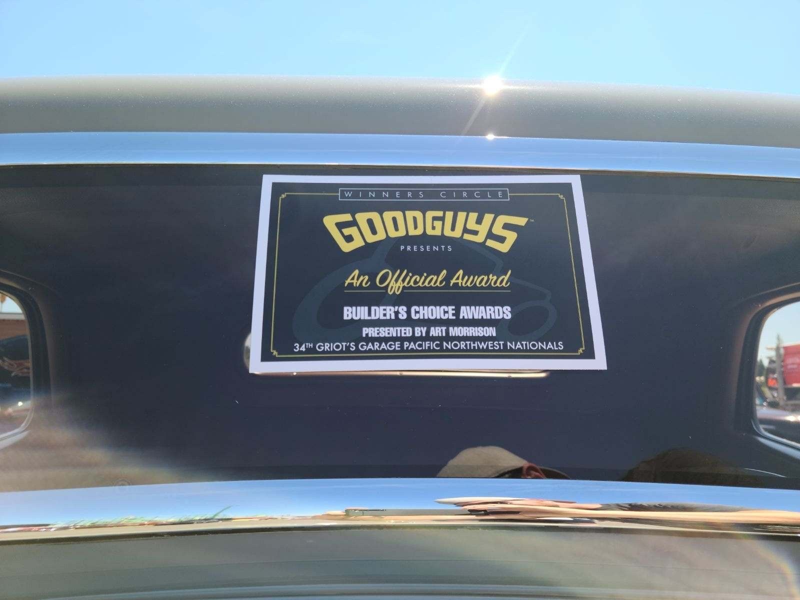 Goodguys car show sticker on a car windshield, with a blue sky reflected above.