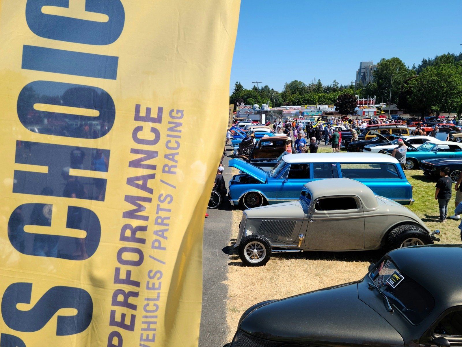 Classic car show with a yellow “CHOICE” banner, featuring vintage cars on a sunny grassy field.