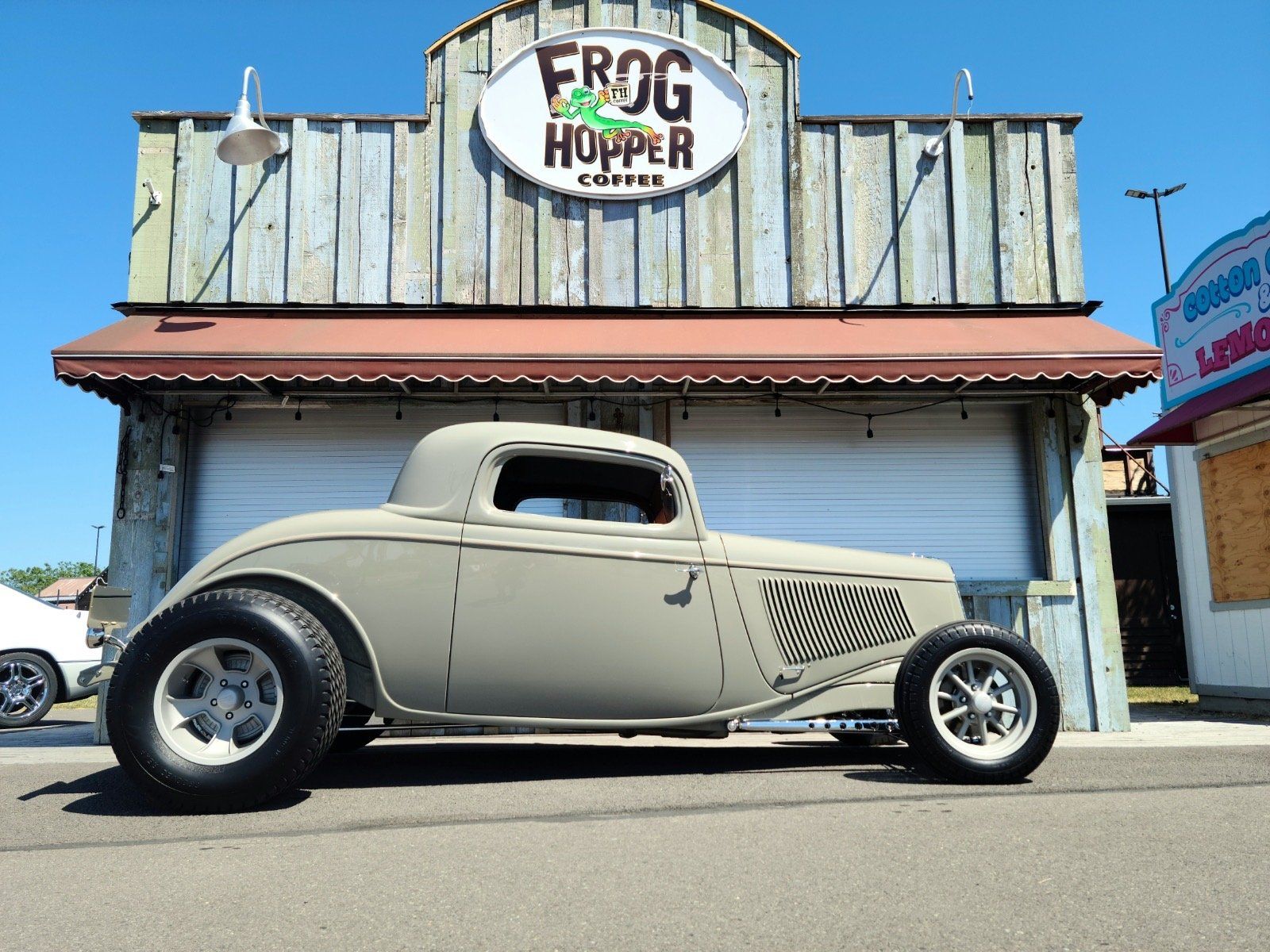 Vintage beige hot rod parked outside Frog Hopper storefront on a sunny day