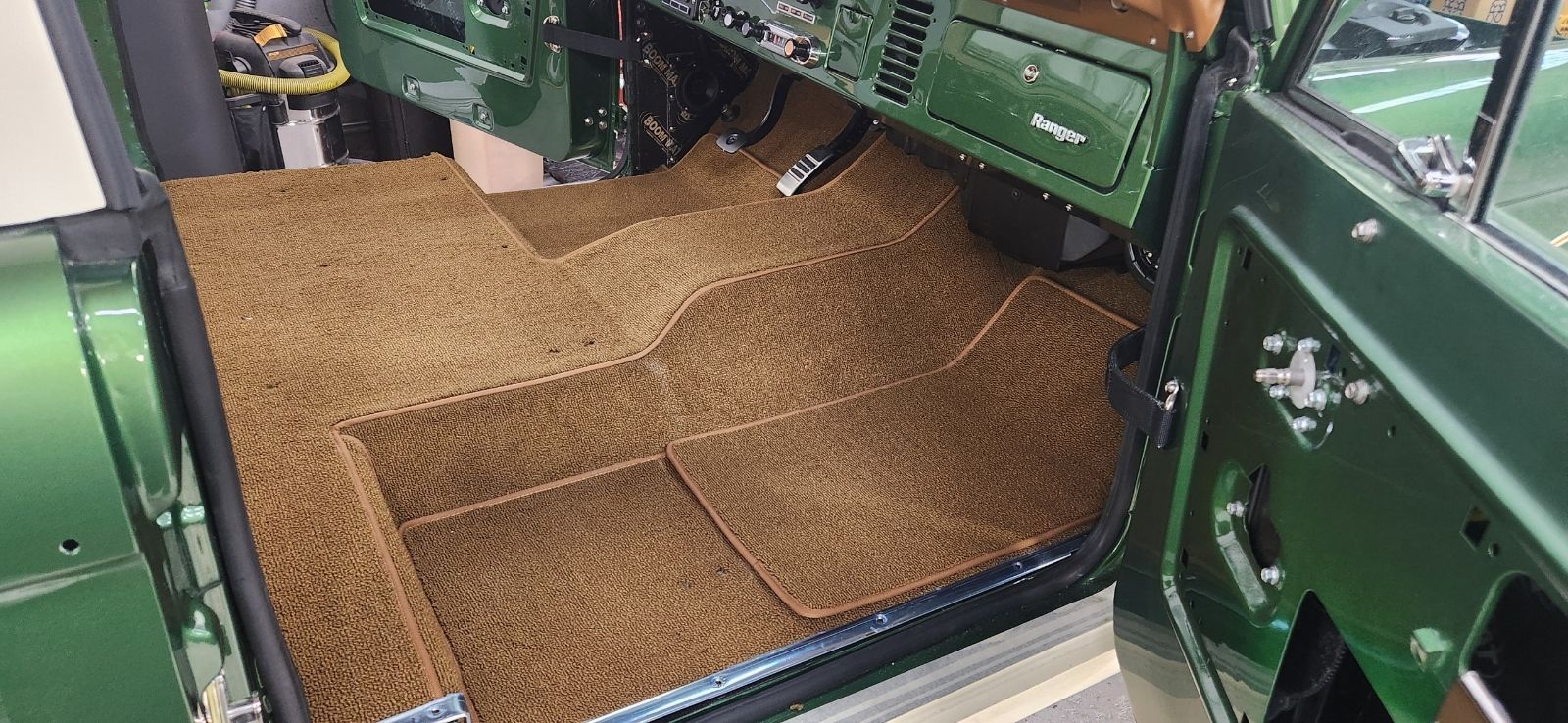 Green off-road vehicle interior with tan quilted floor mats and open door panels
