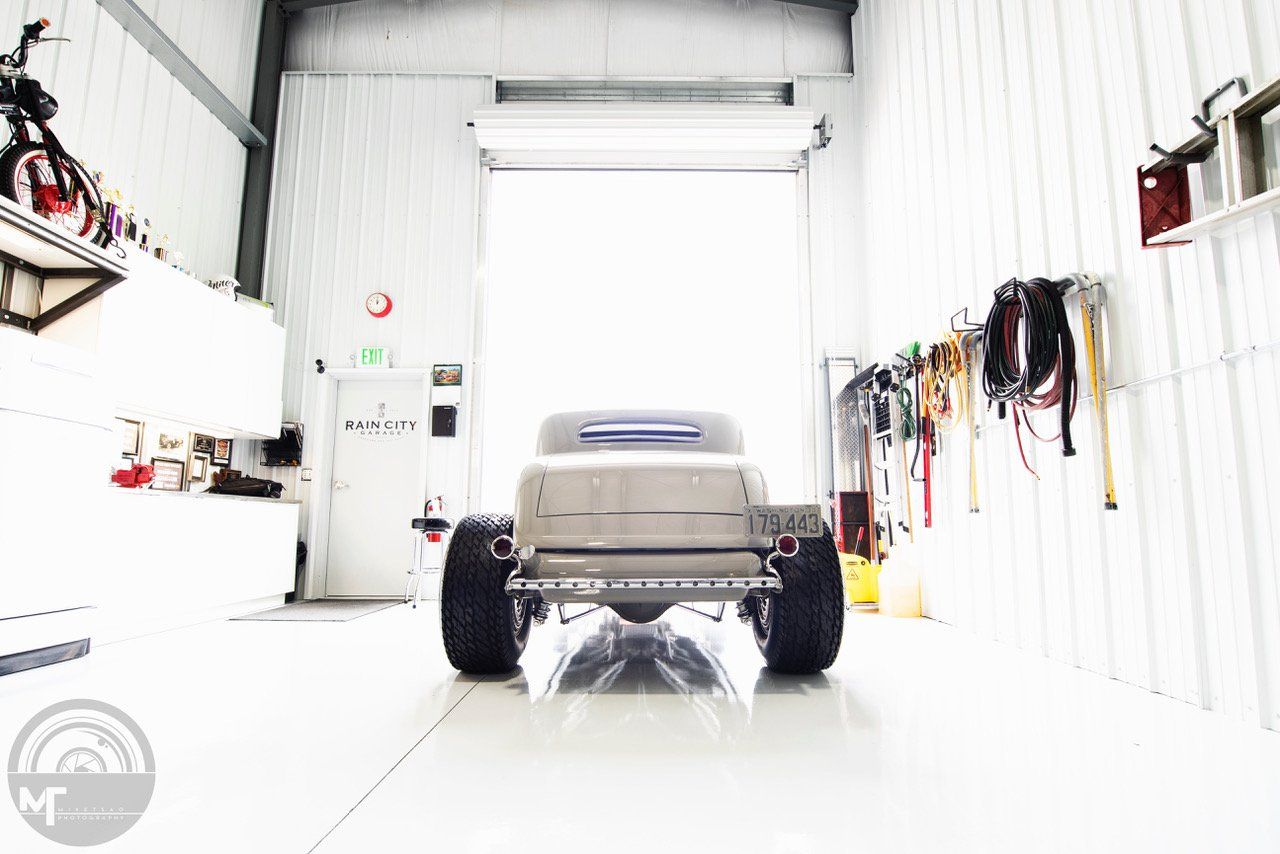 Small gray utility vehicle in a bright white garage with large black wheels and tools on the walls