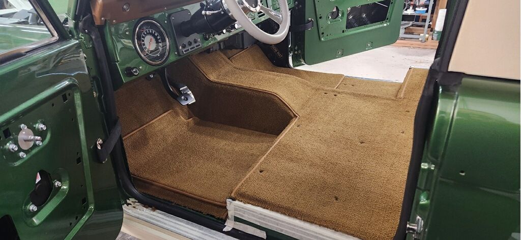 Green vintage car interior with tan carpet and open door, showing the driver’s seat area and dashboard