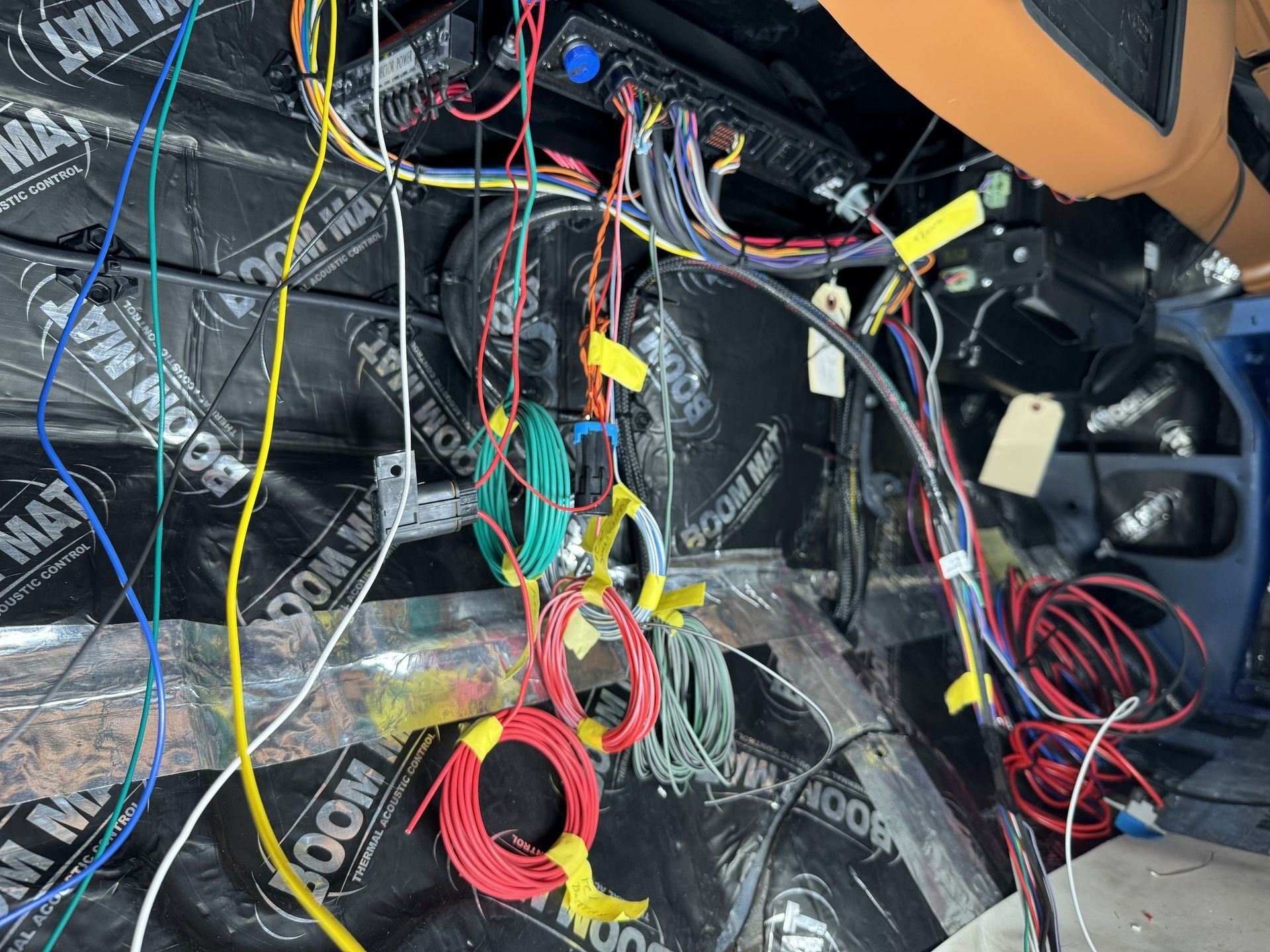 Car dashboard wiring exposed behind trim, with tangled multicolored cables and insulation panels.