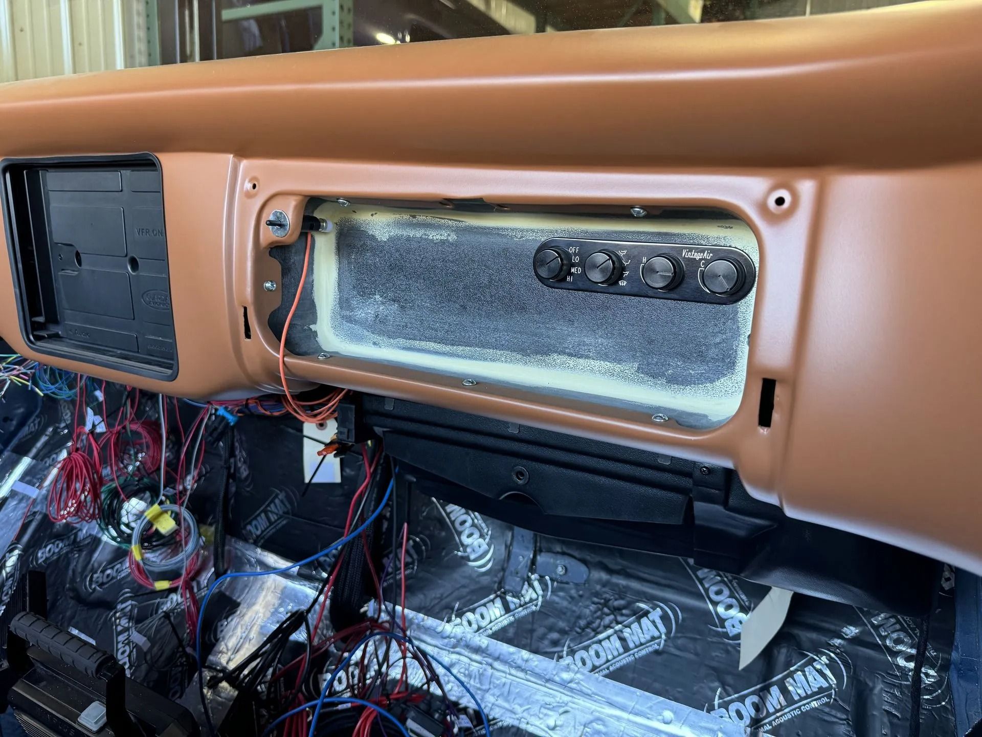 Car dashboard stripped open, exposing wiring, vents, and a frosted display panel during repair.