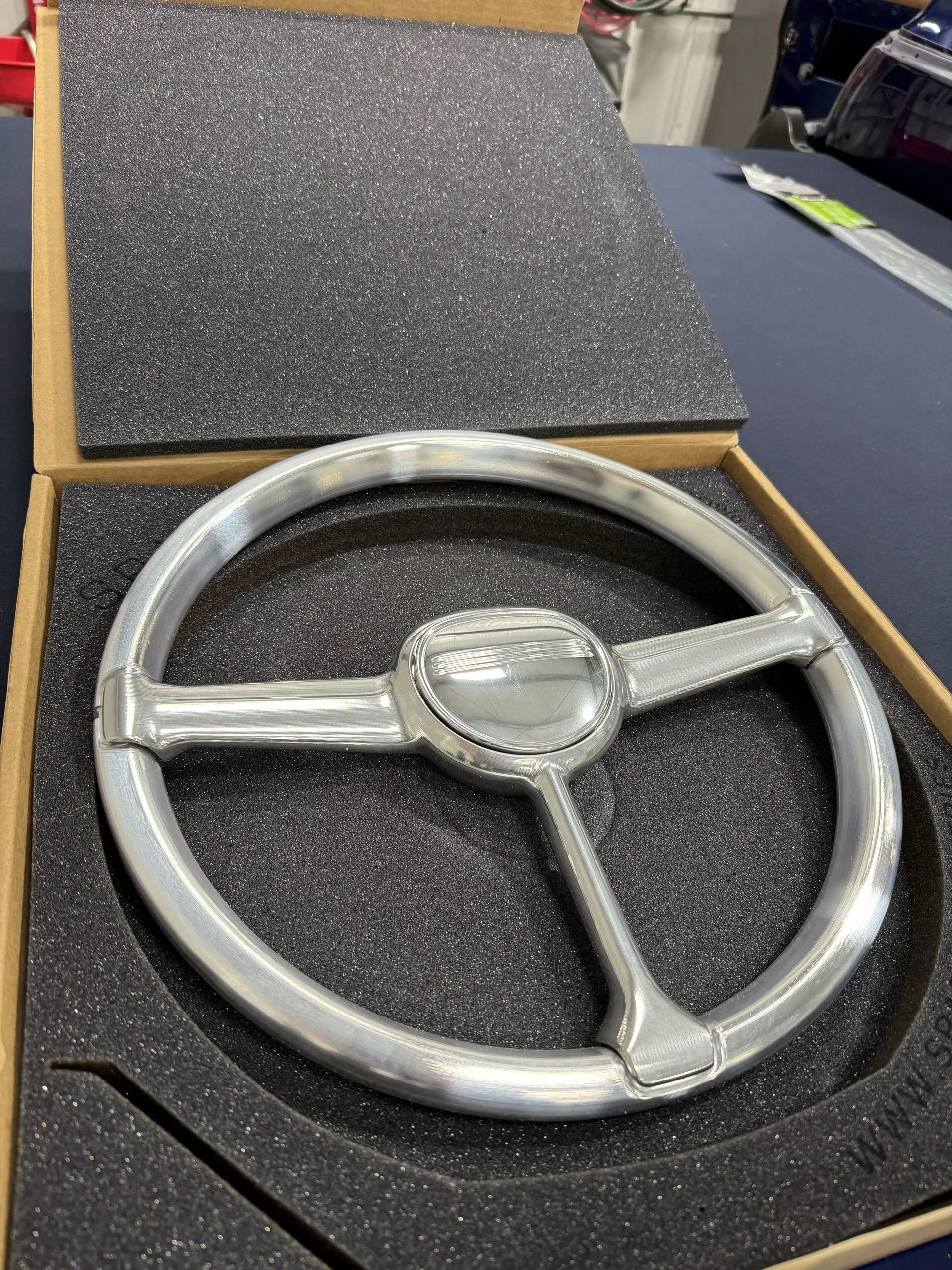 Silver steering wheel in a black foam-lined box, viewed from above.