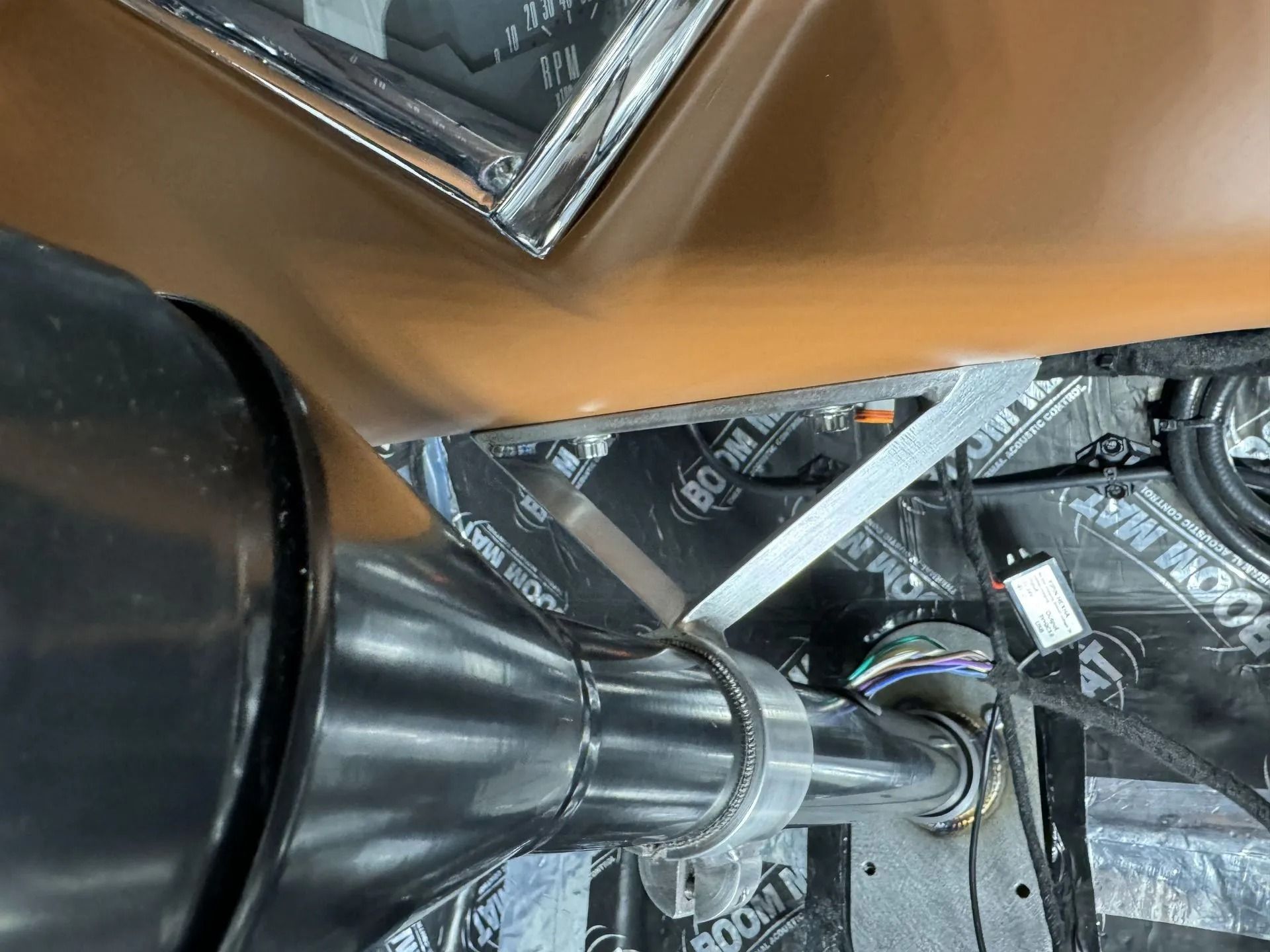 Black hose and metal ductwork beneath a tan surface, with wires and reflective insulation visible