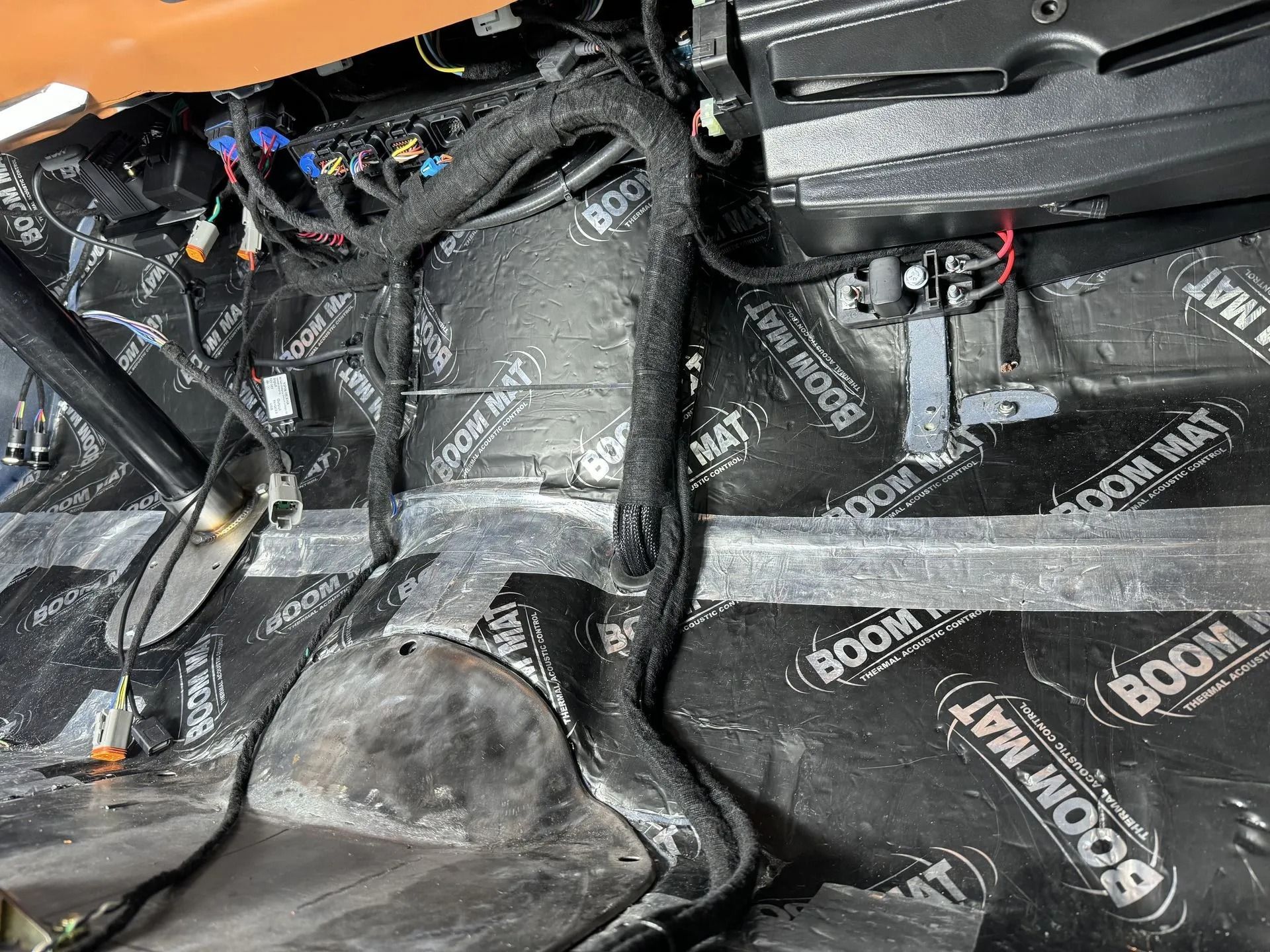 Car interior floor covered in black sound-deadening material and exposed wiring under the dashboard