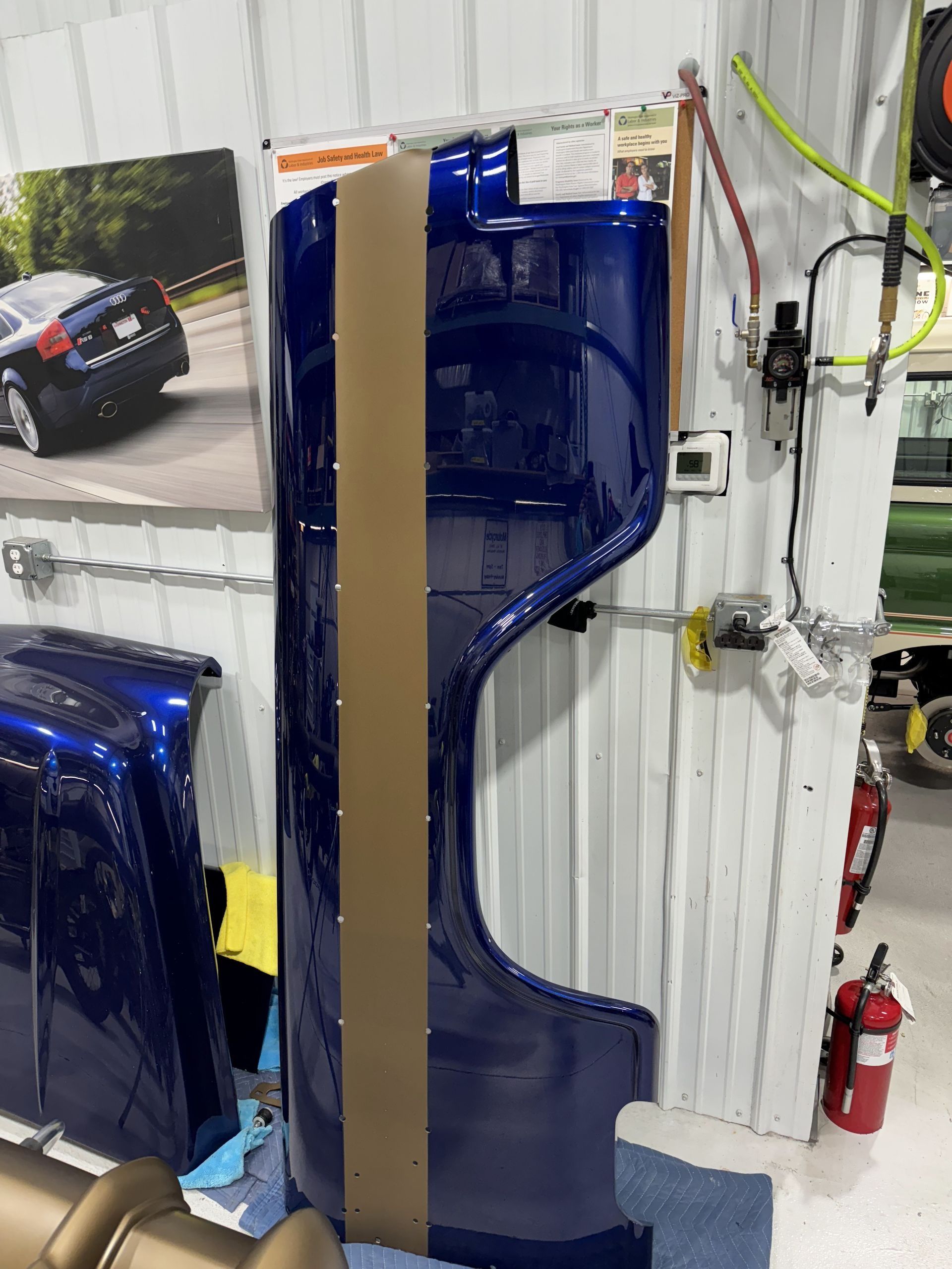 Blue vehicle body panel taped upright in a workshop with tools and a fire extinguisher nearby