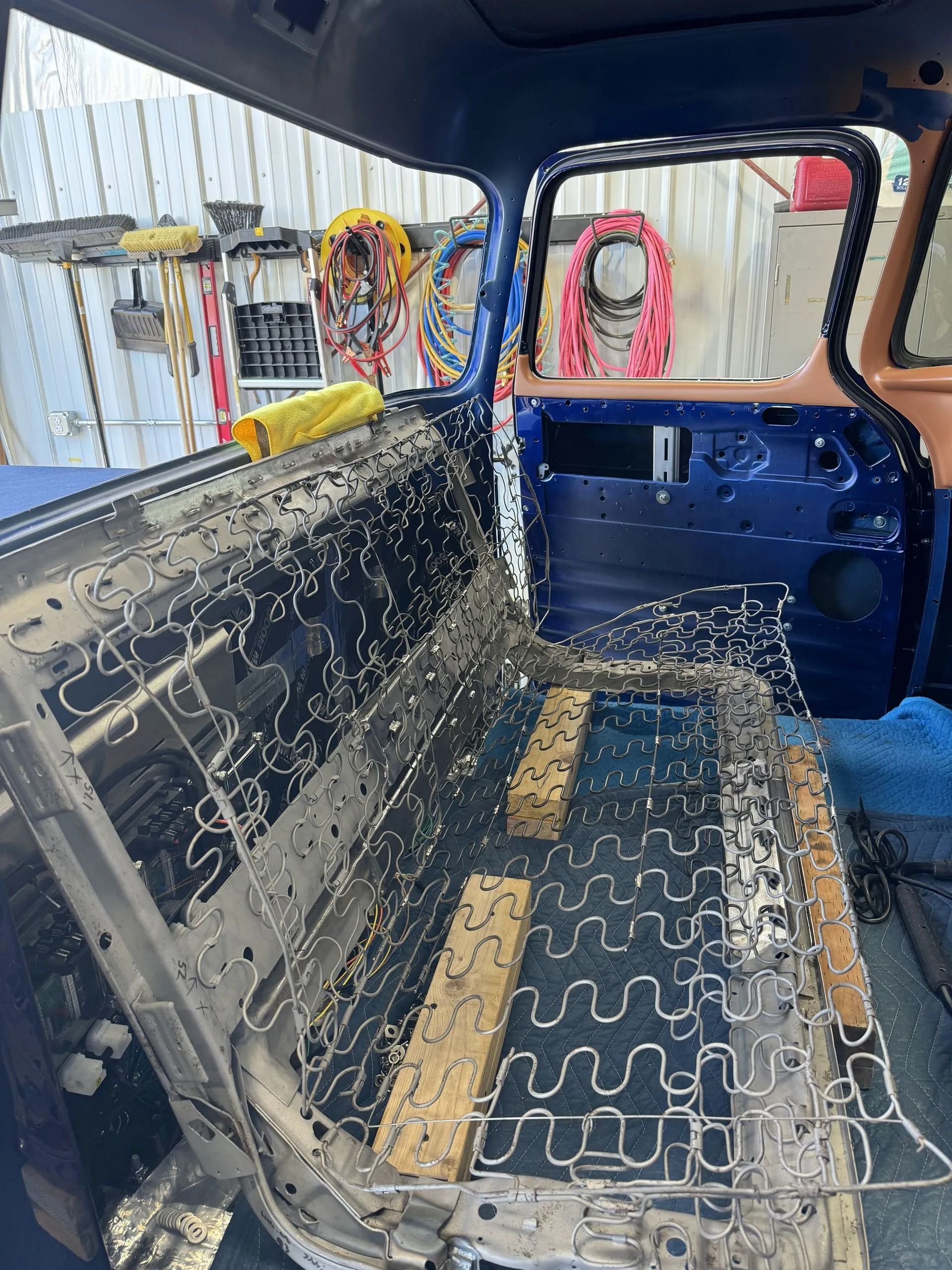 Inside a car with exposed seats and patchwork upholstery, viewed from the back seat area