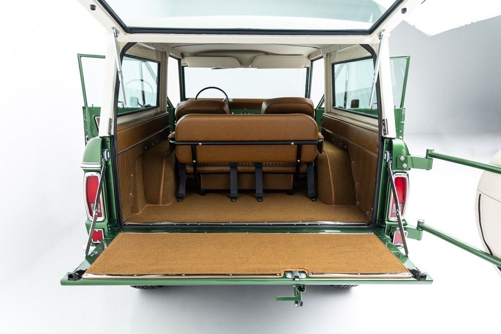 Open rear view of a green vintage vehicle with tan interior seats and folded-down tailgate.