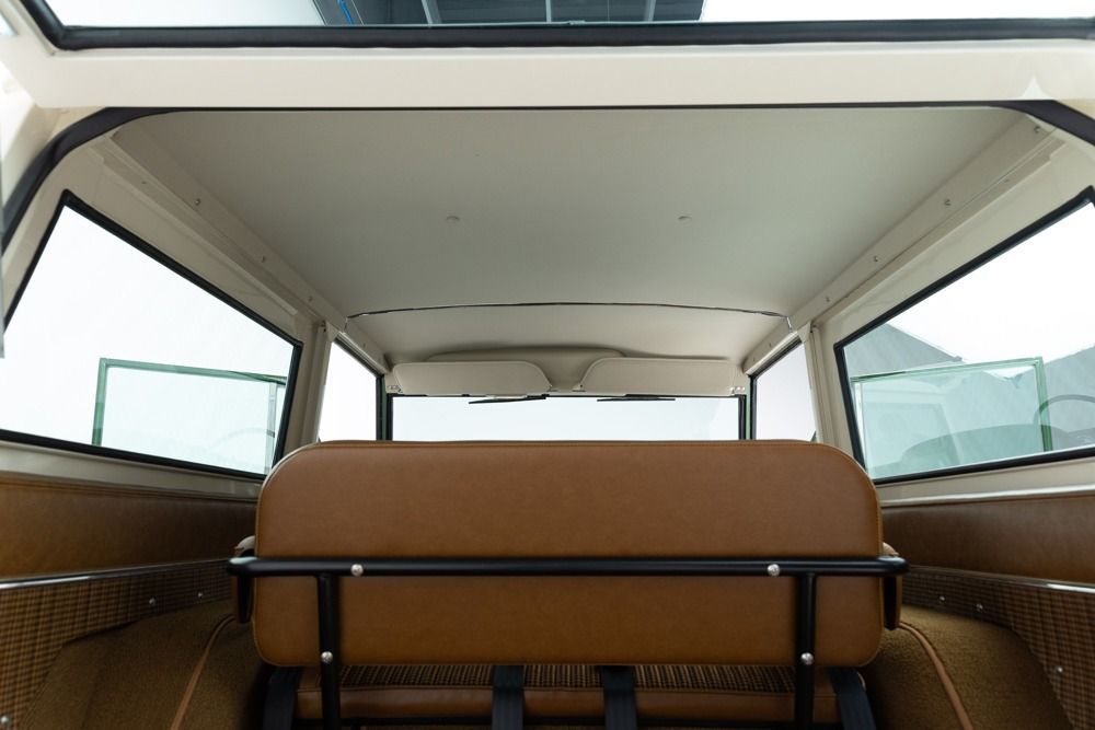 Interior of a vintage car with tan seats and open windows, viewed from the back seat