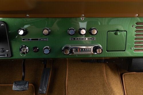 Vintage green car dashboard with analog radio, knobs, and pedal controls under the dash