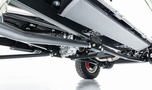 Undercarriage of a vehicle with metal frame rails and a visible rear wheel on a white background