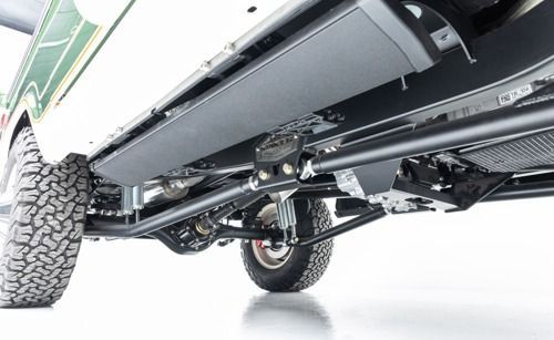 Undercarriage view of an off-road vehicle with suspension, drivetrain, and large rugged tires visible