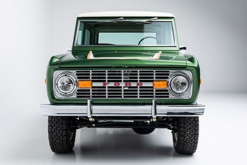 Front view of a green vintage off-road SUV with headlights and chrome grille on a white studio background