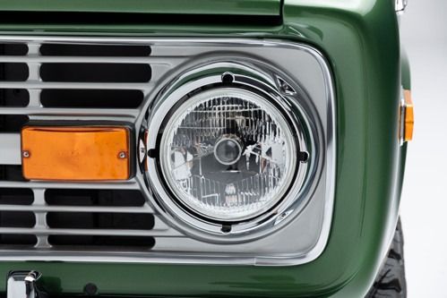 Close-up of a green vintage car front with round headlight and orange turn signal