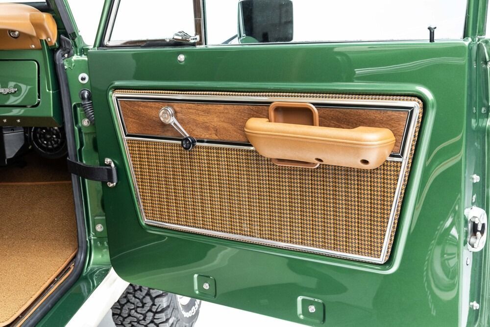 Green vintage car door with tan armrest, woven panel, and black handle open in view