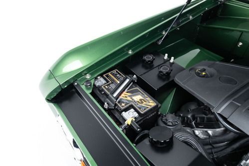 Close-up of a green car engine bay with the battery and air intake visible