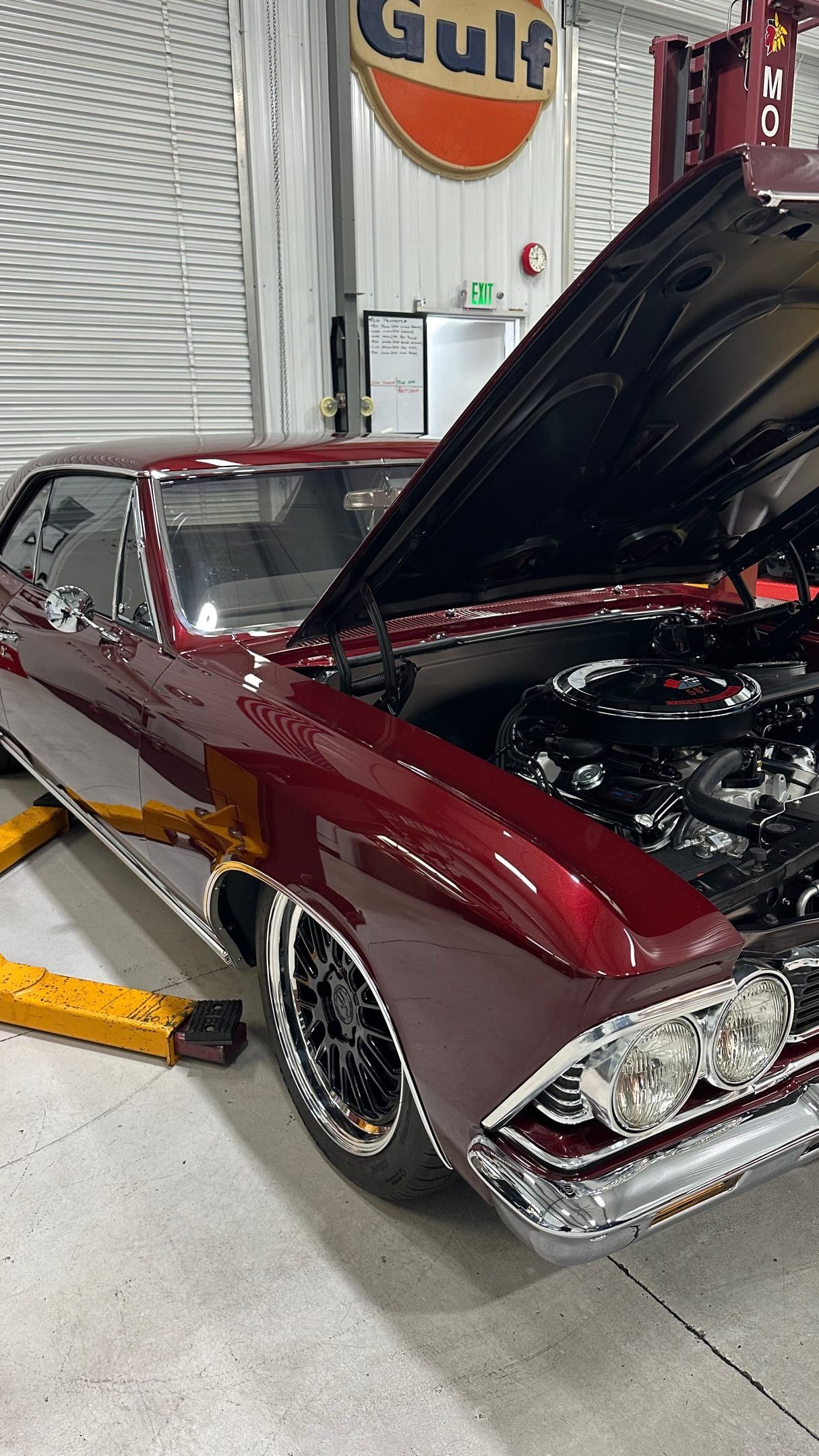 Maroon classic car with hood open in a garage, showing a polished chrome grille and racing-style wheels