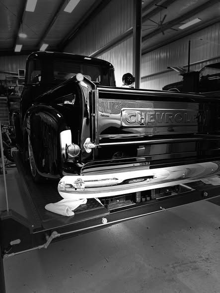 Black classic Chevrolet pickup truck in a garage, rear view with chrome bumper and tailgate.