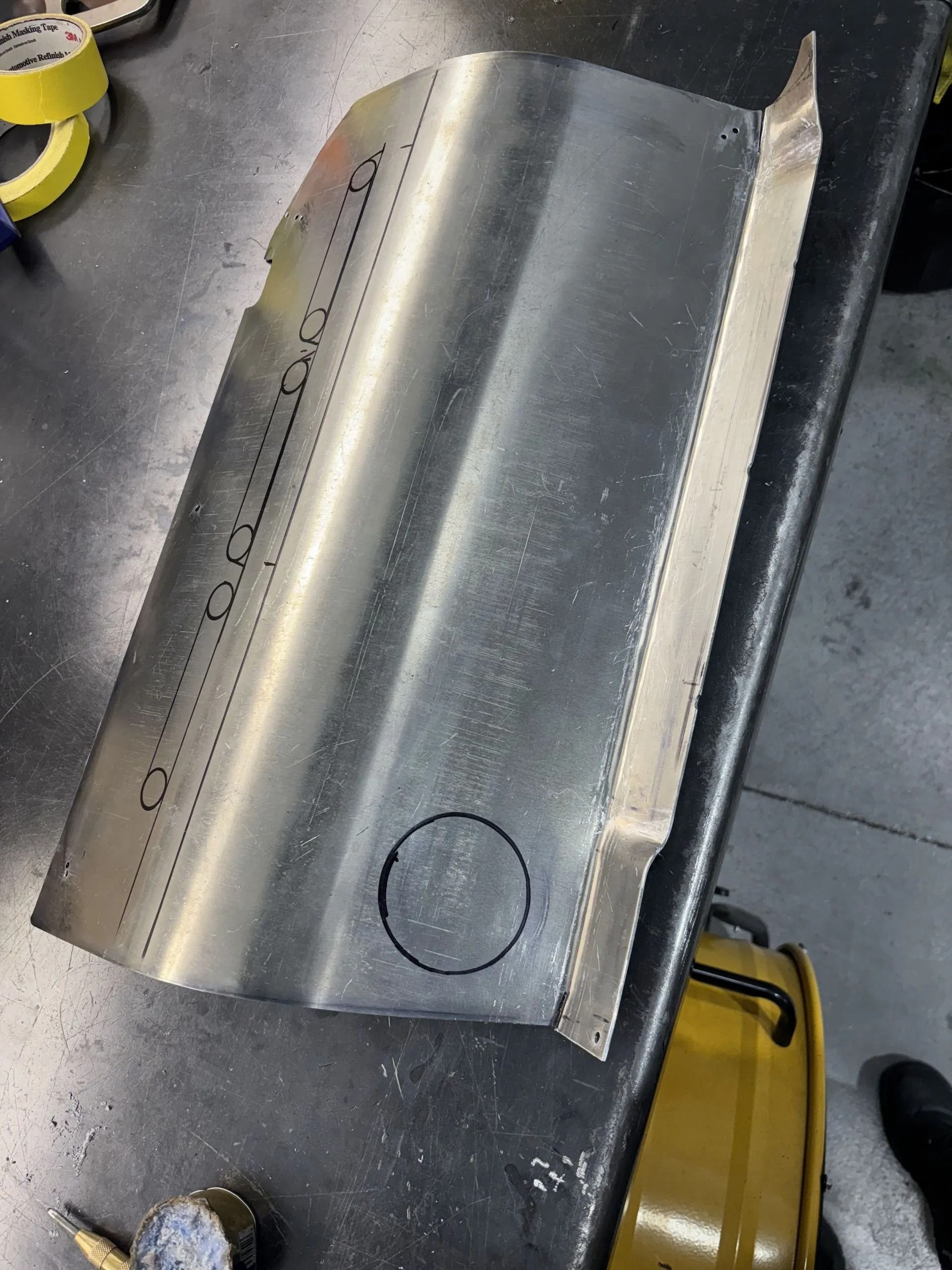 Metal sheet with a curved bend and circular cutout on a workshop floor, viewed from above