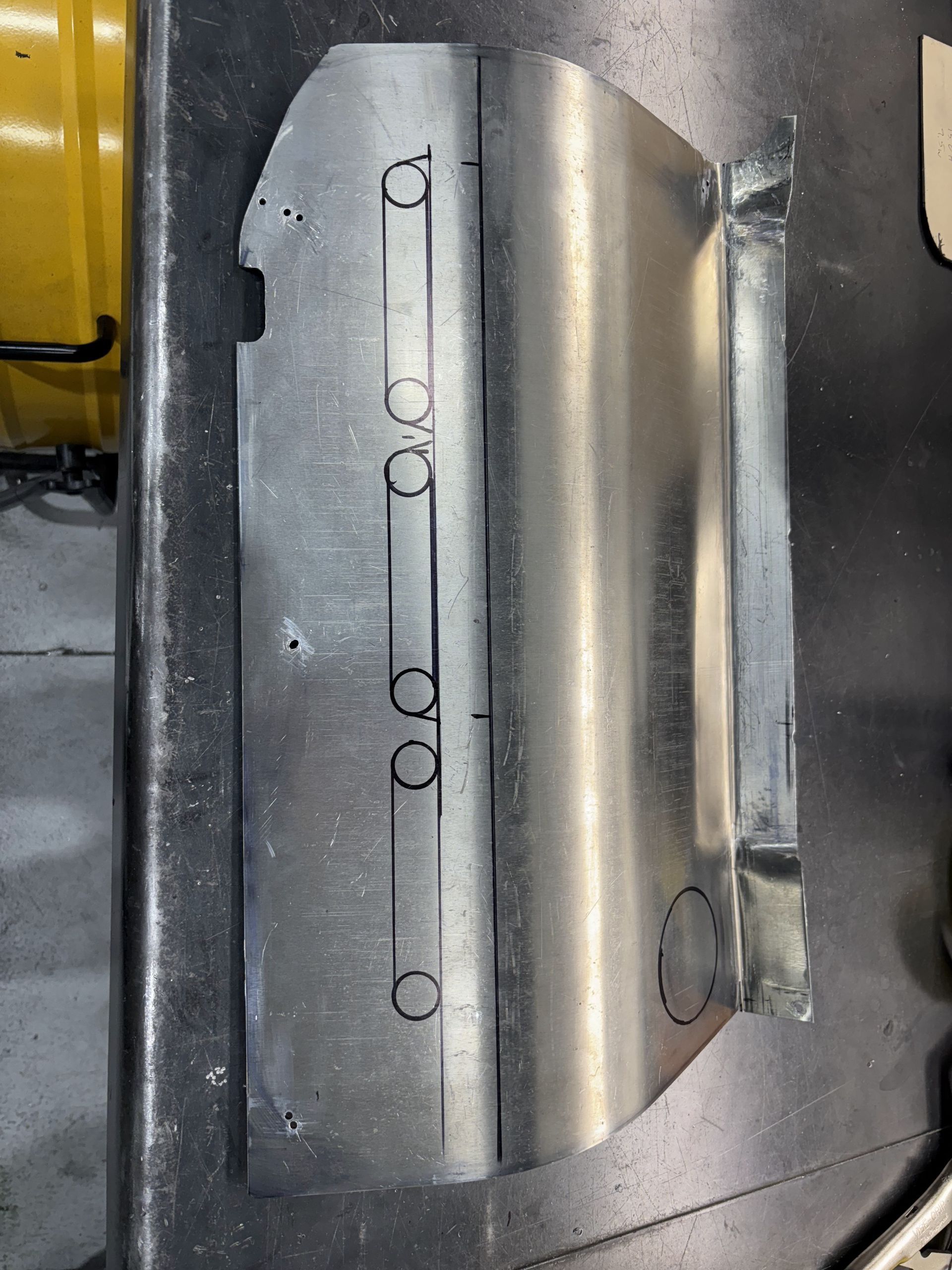 Close-up of a metal machine part with circular holes and a curved brushed surface.