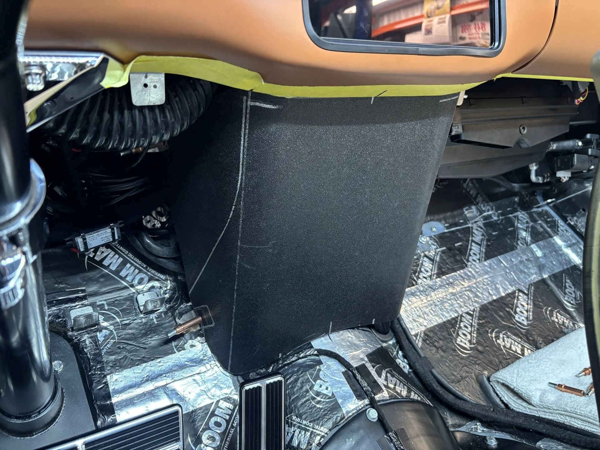 Car interior floor with black carpet and tan dashboard trim, showing the center tunnel and footwell area.