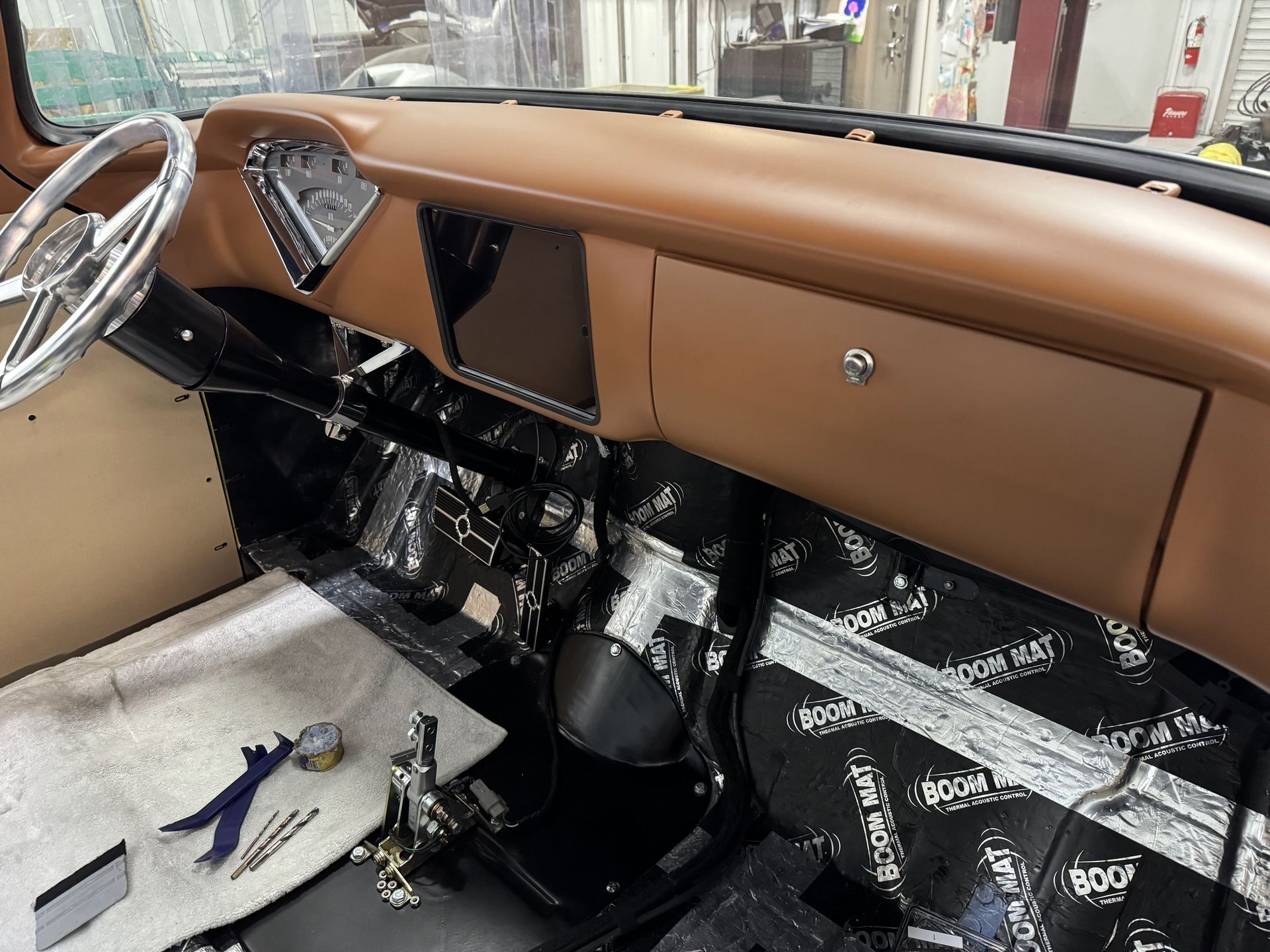 Vintage car interior with tan dashboard, black floor, and exposed wiring during restoration