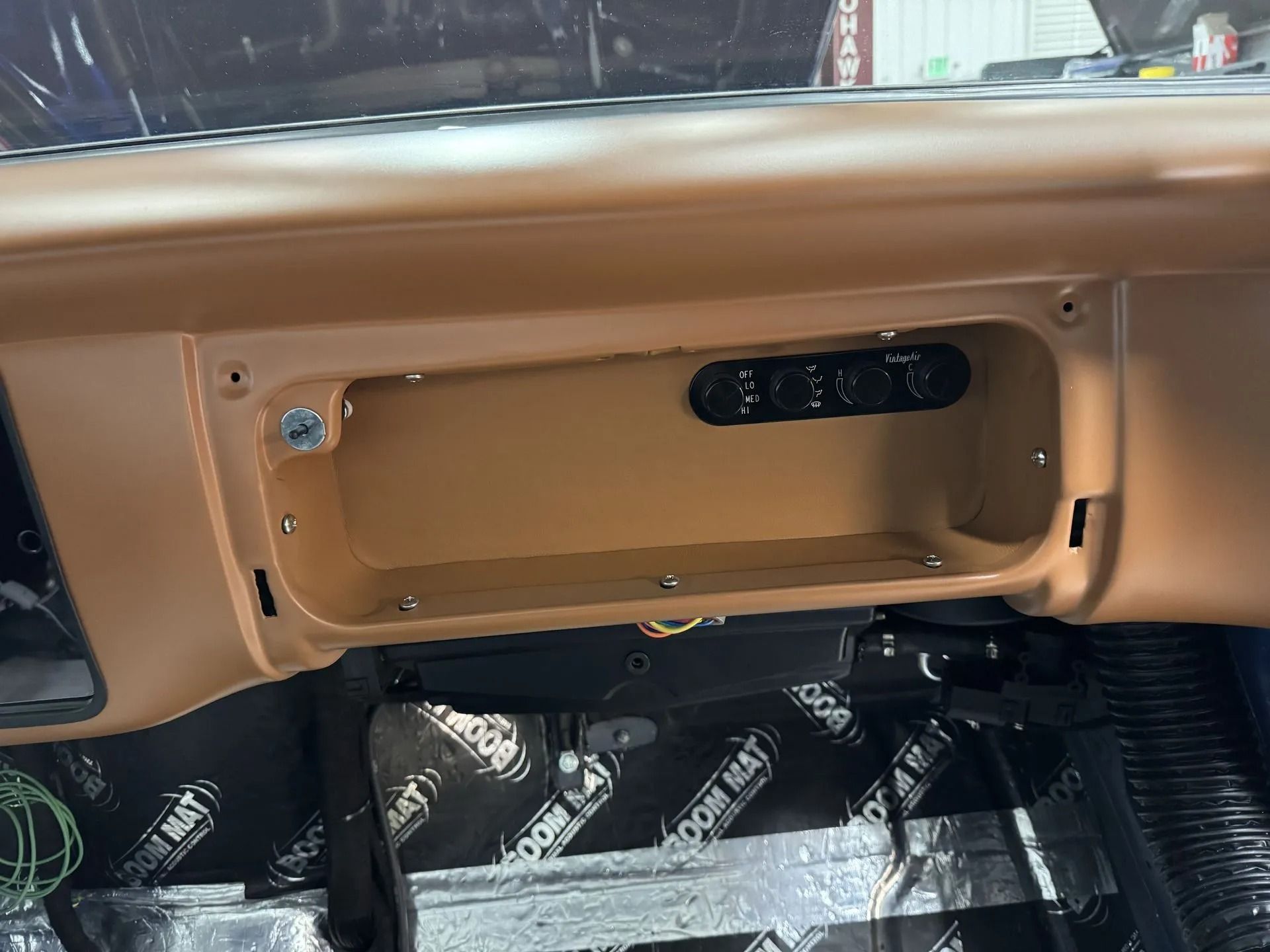 Tan dashboard panel with an open glovebox cavity and exposed wiring beneath the glove compartment