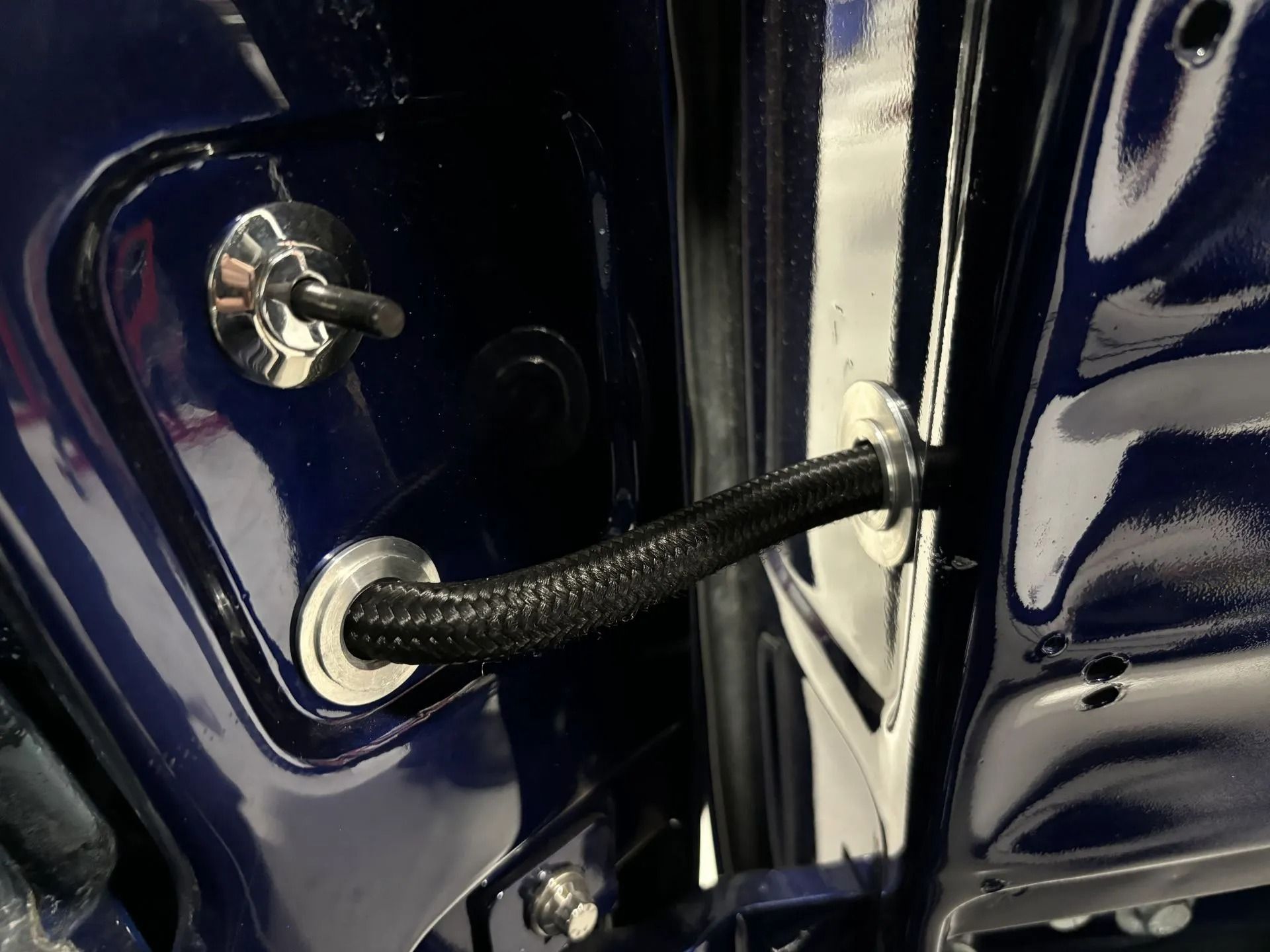 Black braided wiring harness in a car door jamb with a metal mounting stud and blue paint.