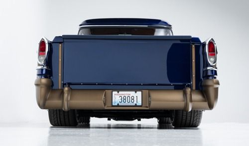 Rear view of a dark blue vintage car with tan bumpers and a white license plate on a plain white background
