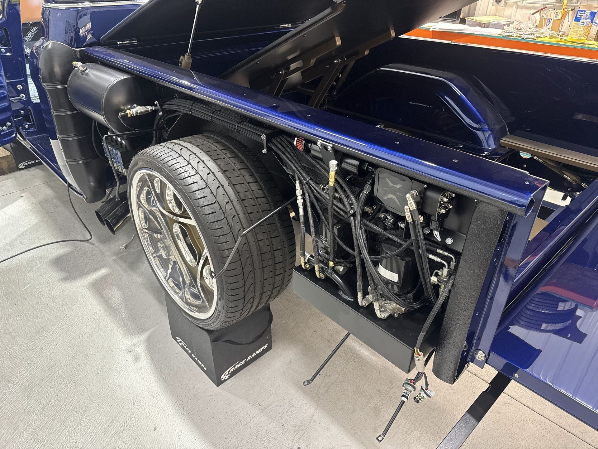 Blue vehicle chassis with exposed rear wheel and engine components on display platform