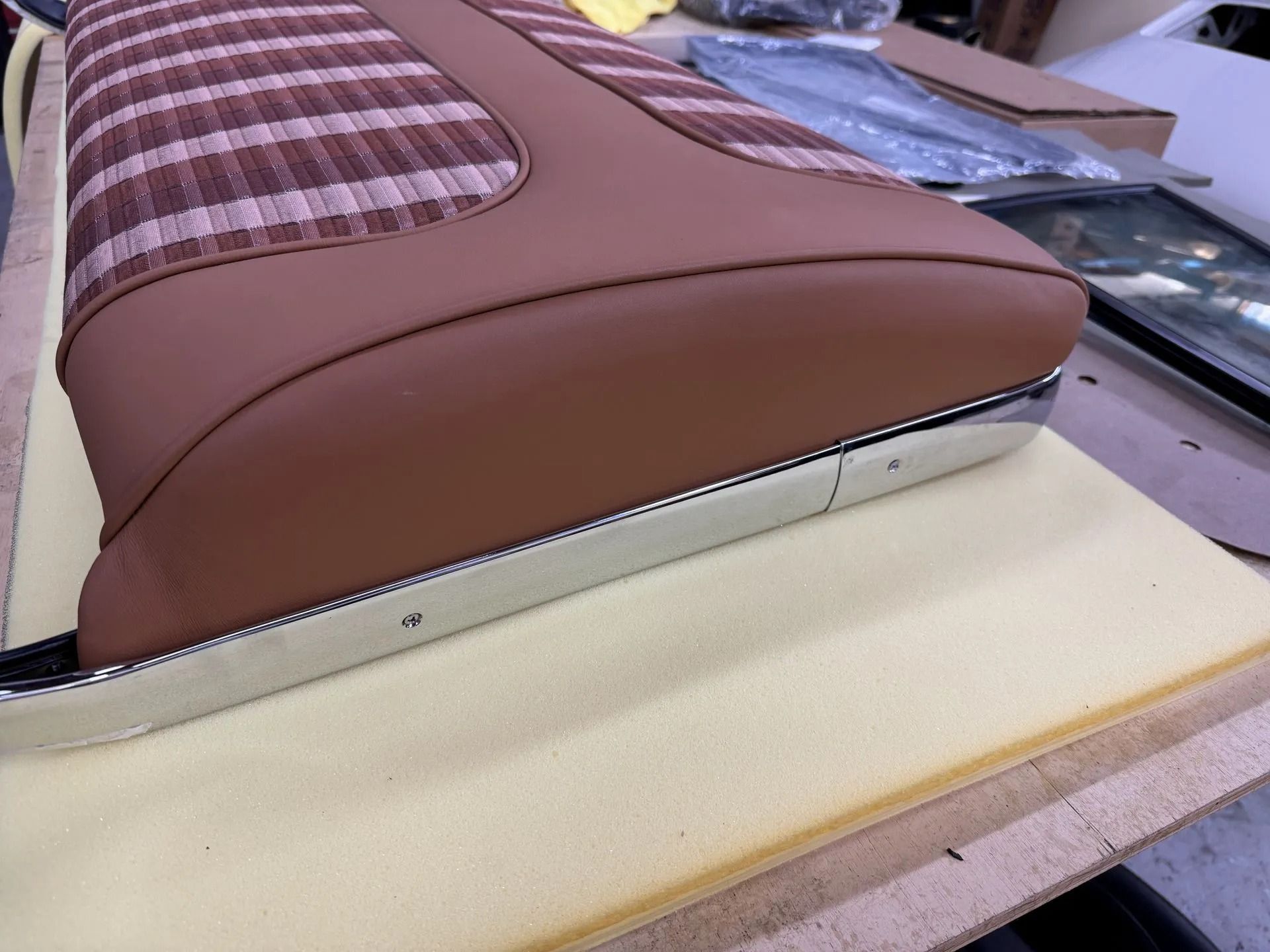 Close-up of a brown upholstered cushion with plaid fabric, resting on a cream foam base in a workshop.